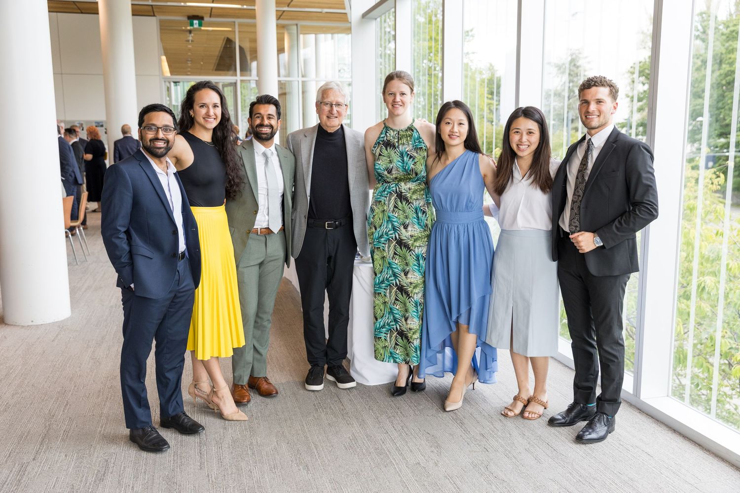 Group of eight professionally dressed colleagues smiling together at a bright modern venue.