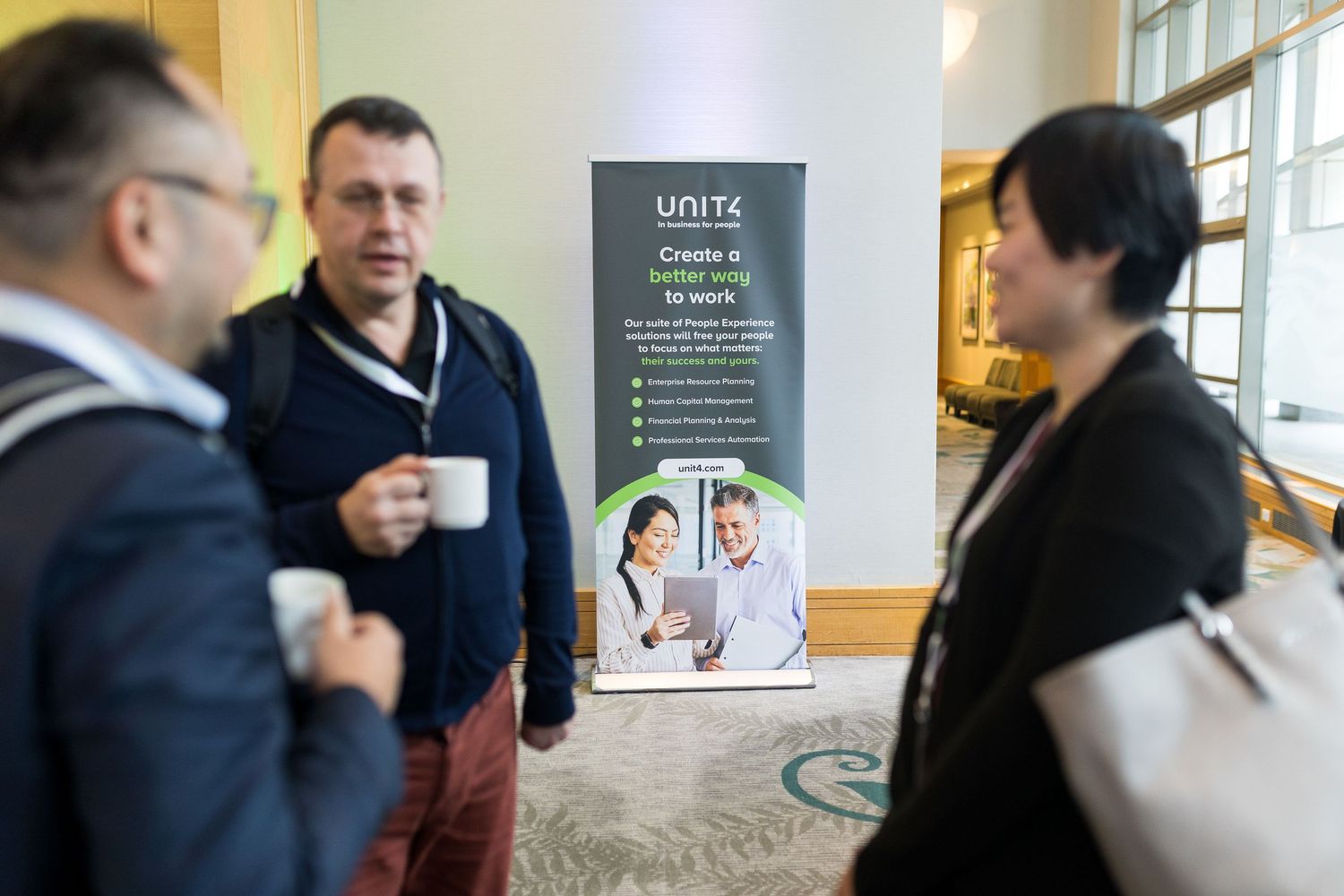 Three professionals networking at a Unite conference event, conversing near a branded banner display held at the Fairmont Waterfront Hotel.