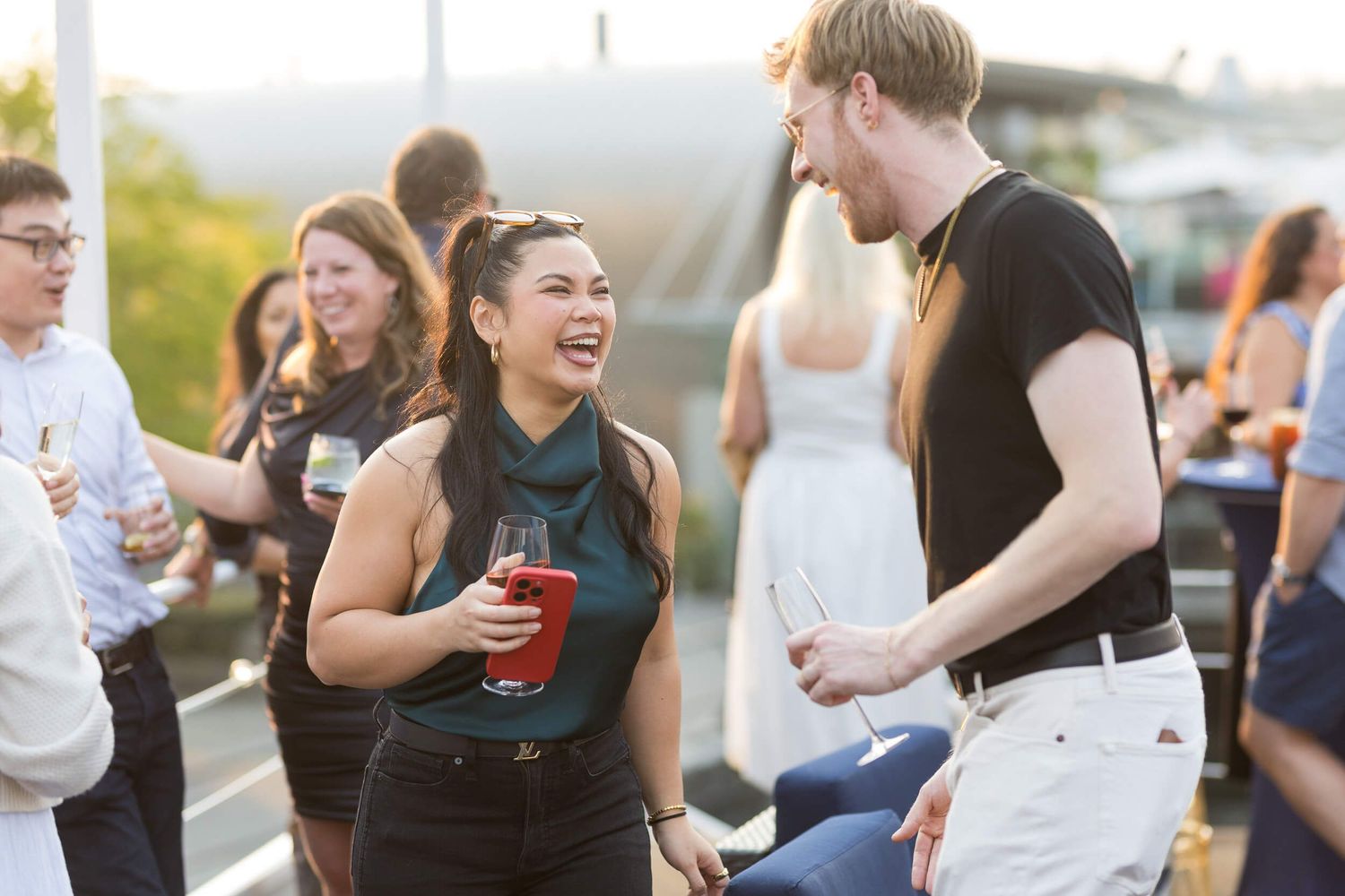 People socializing at a rooftop party, laughing and holding drinks at an outdoor evening event.