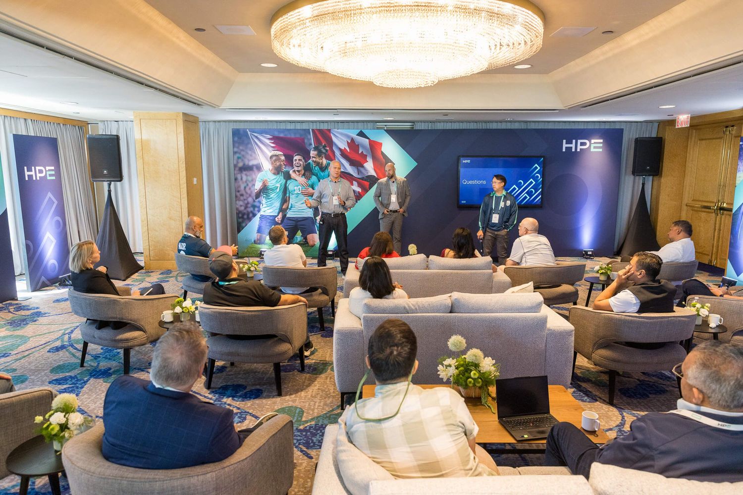 HPE corporate event with presenters on stage addressing seated audience in an elegant hotel conference room.