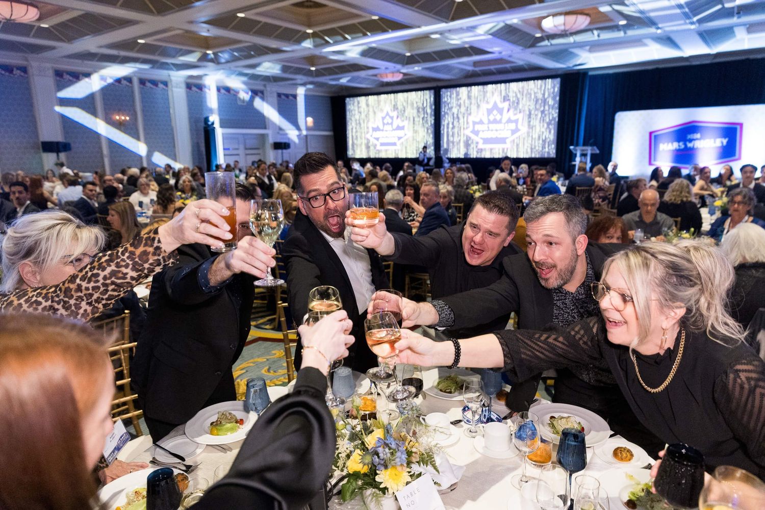 Group of attendees raising glasses in a celebratory toast at a formal gala dinner event held at the Fairmont Hotel Vancouver.