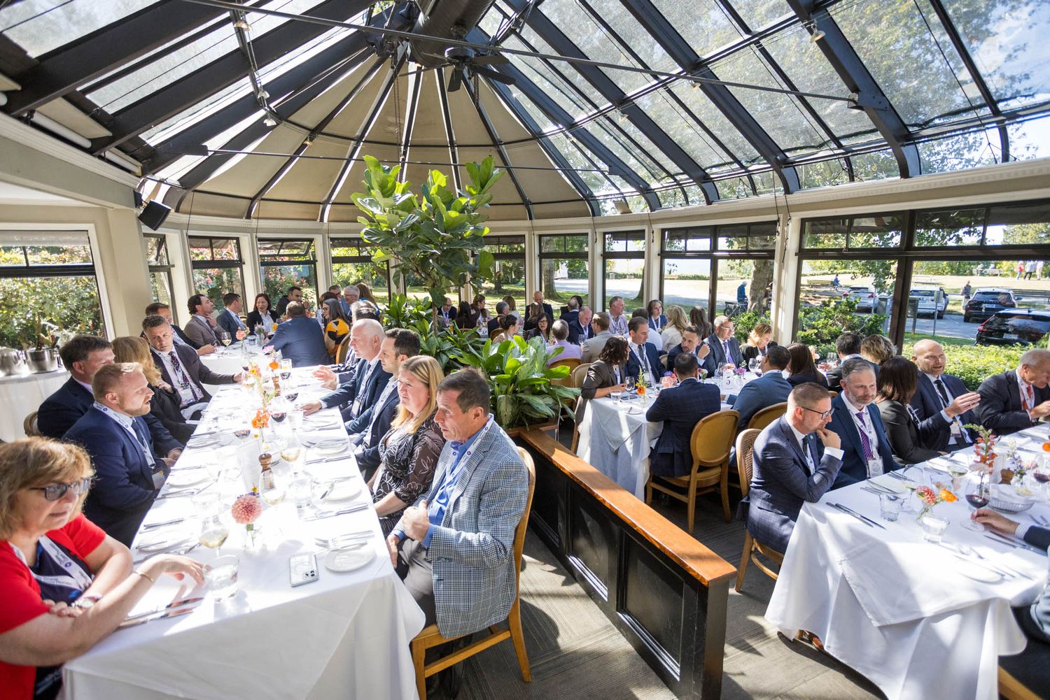 Business professionals dining in an elegant glass-roofed conservatory restaurant during a formal corporate luncheon event.