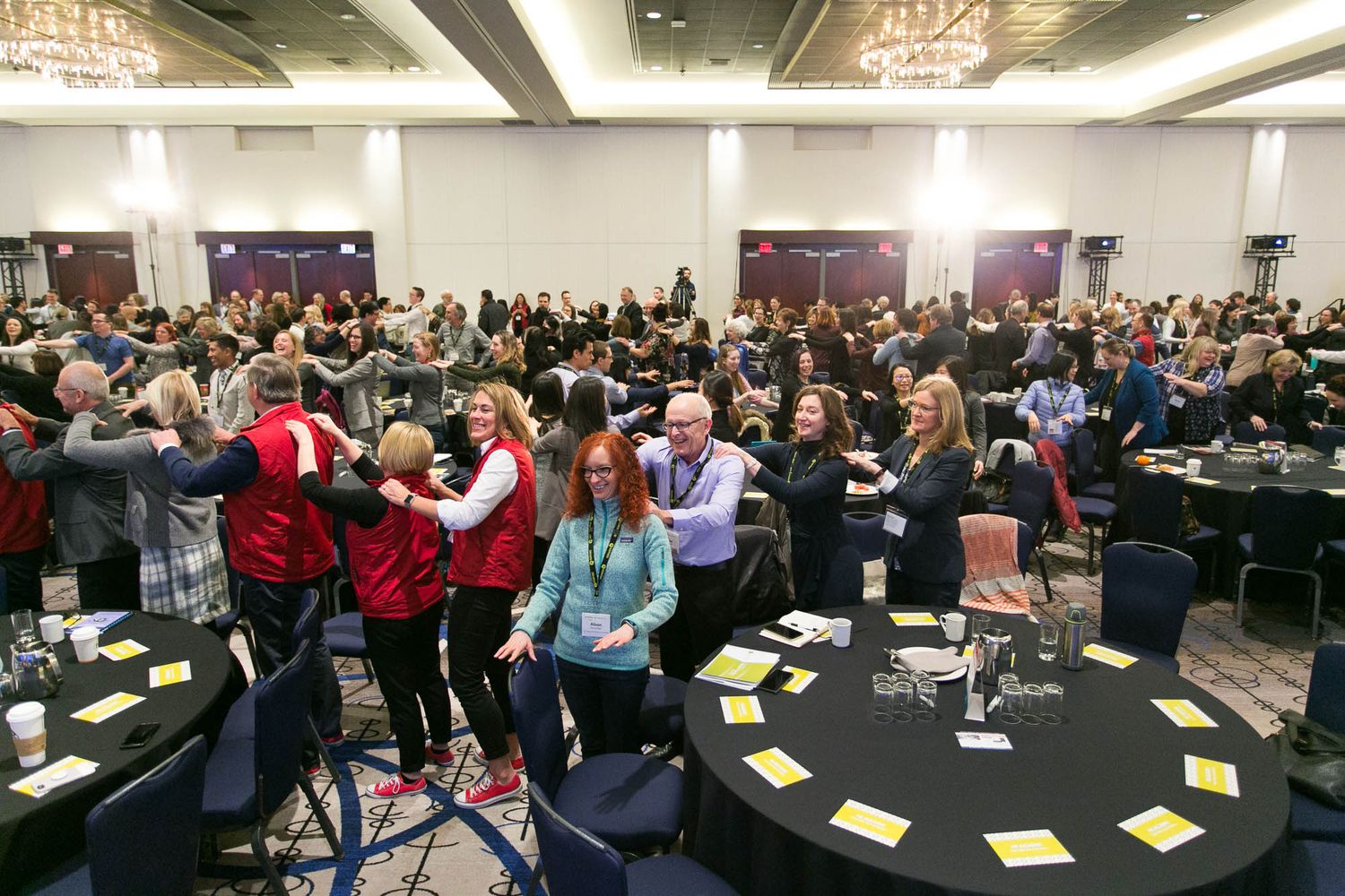 Large conference room at Hyatt Regency Vancouver filled with attendees celebrating and hugging at round tables during the BC Quality Forum.