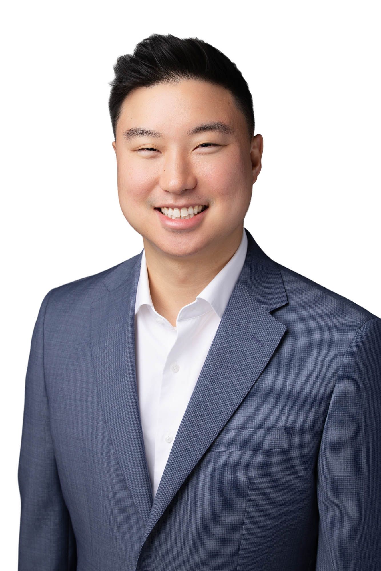 Smiling young professional man in a blue blazer and white shirt poses for a corporate headshot on white background.