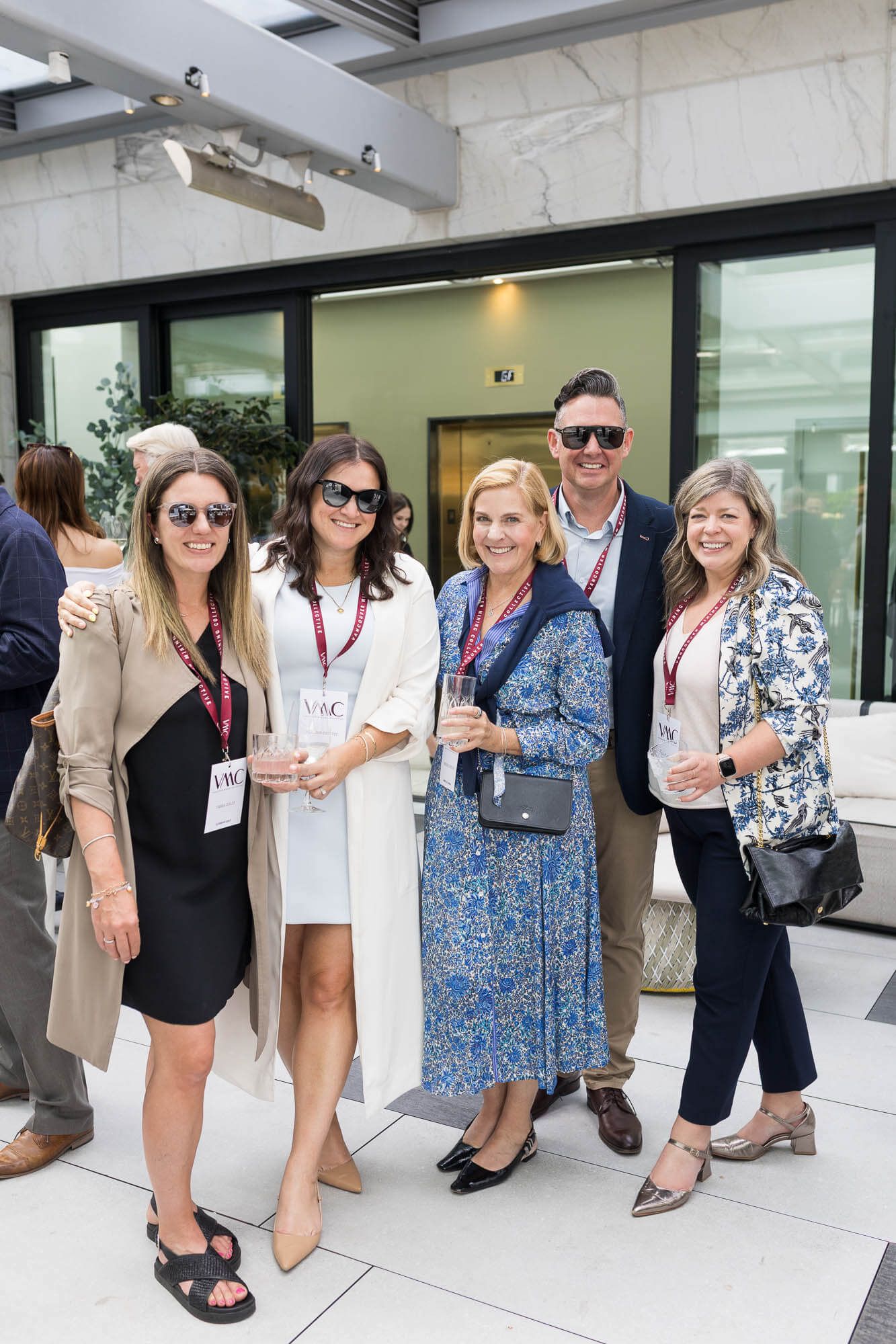 Group of five professionals smiling at an outdoor networking event, wearing lanyards and holding drinks.