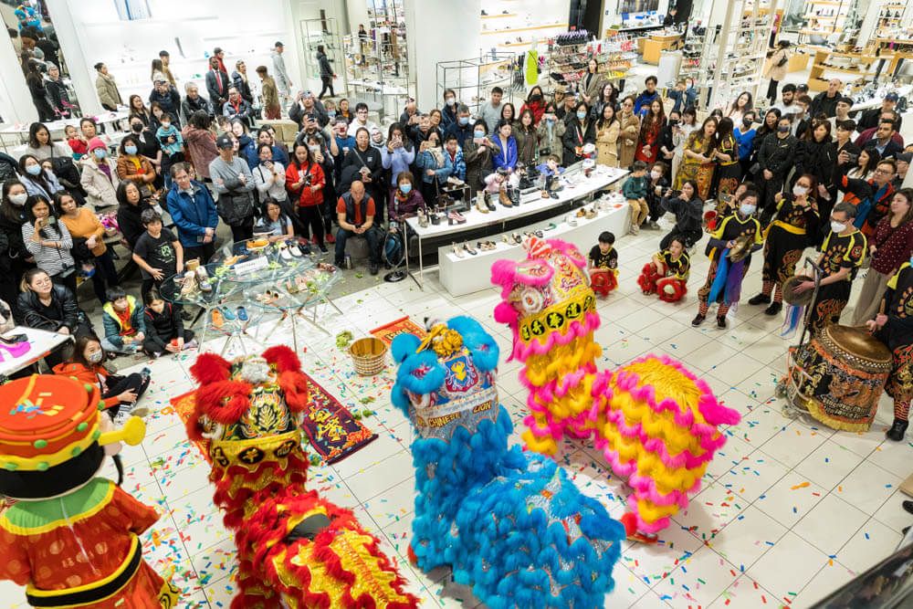 Colorful lion dance performance at a crowded indoor Chinese New Year celebration with confetti and spectators at Pacific Centre.