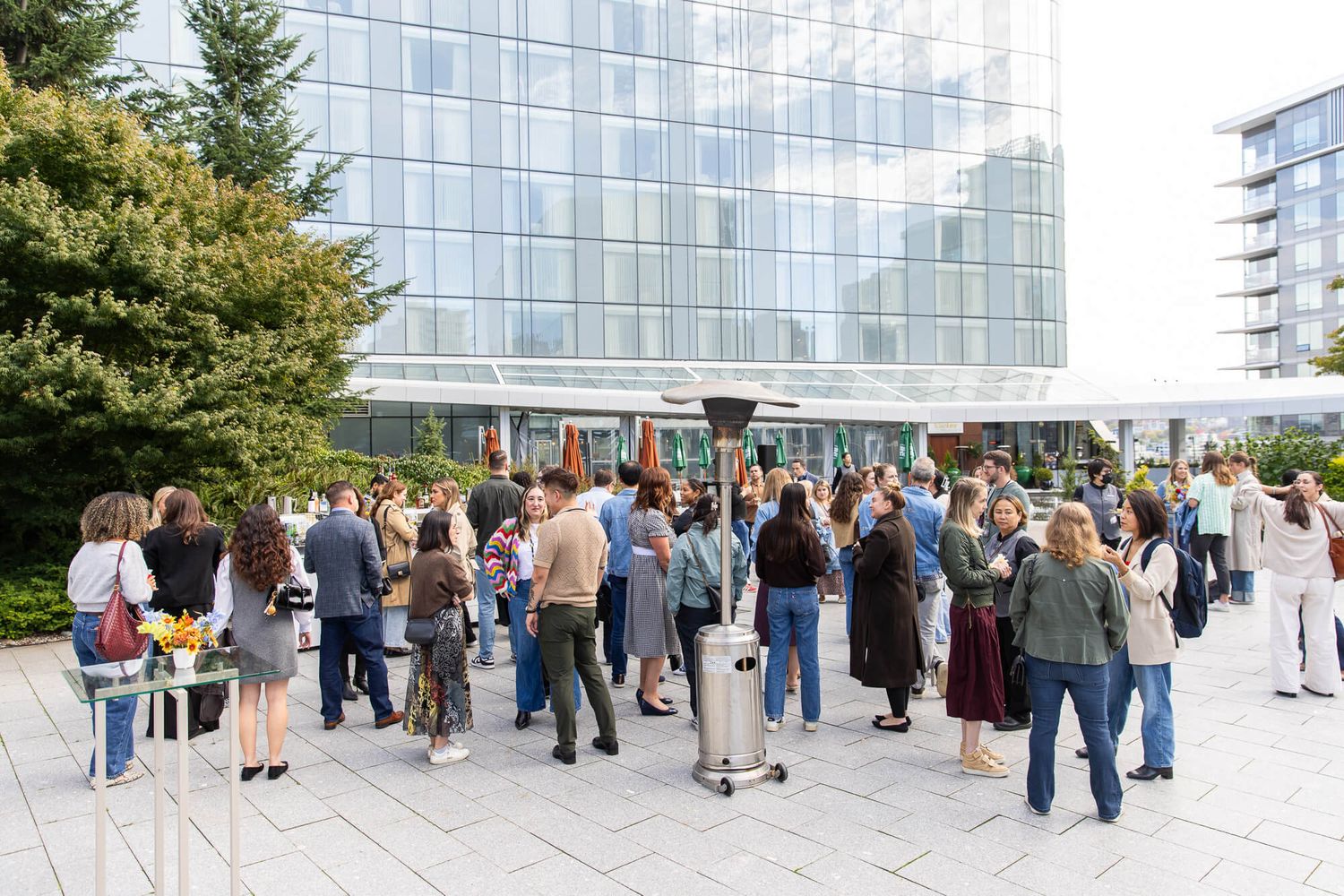 Crowd of professionals networking outdoors at a corporate event near a modern glass office building.
