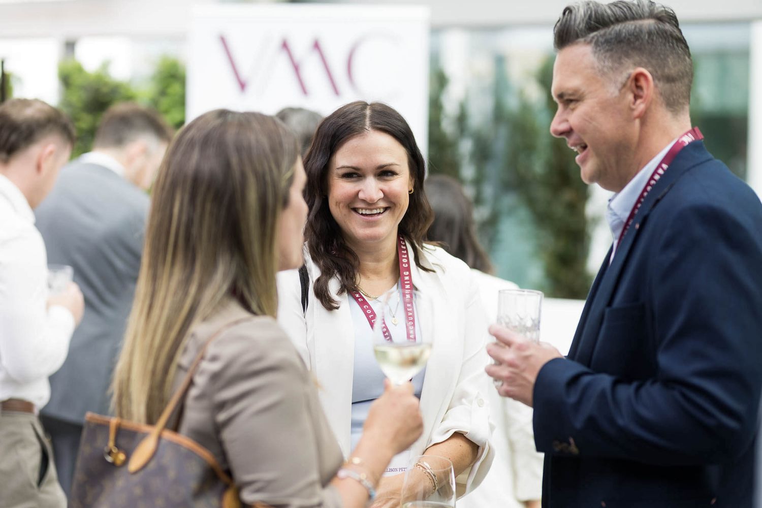 Professionals networking at a corporate event, smiling and conversing in front of a branded backdrop.