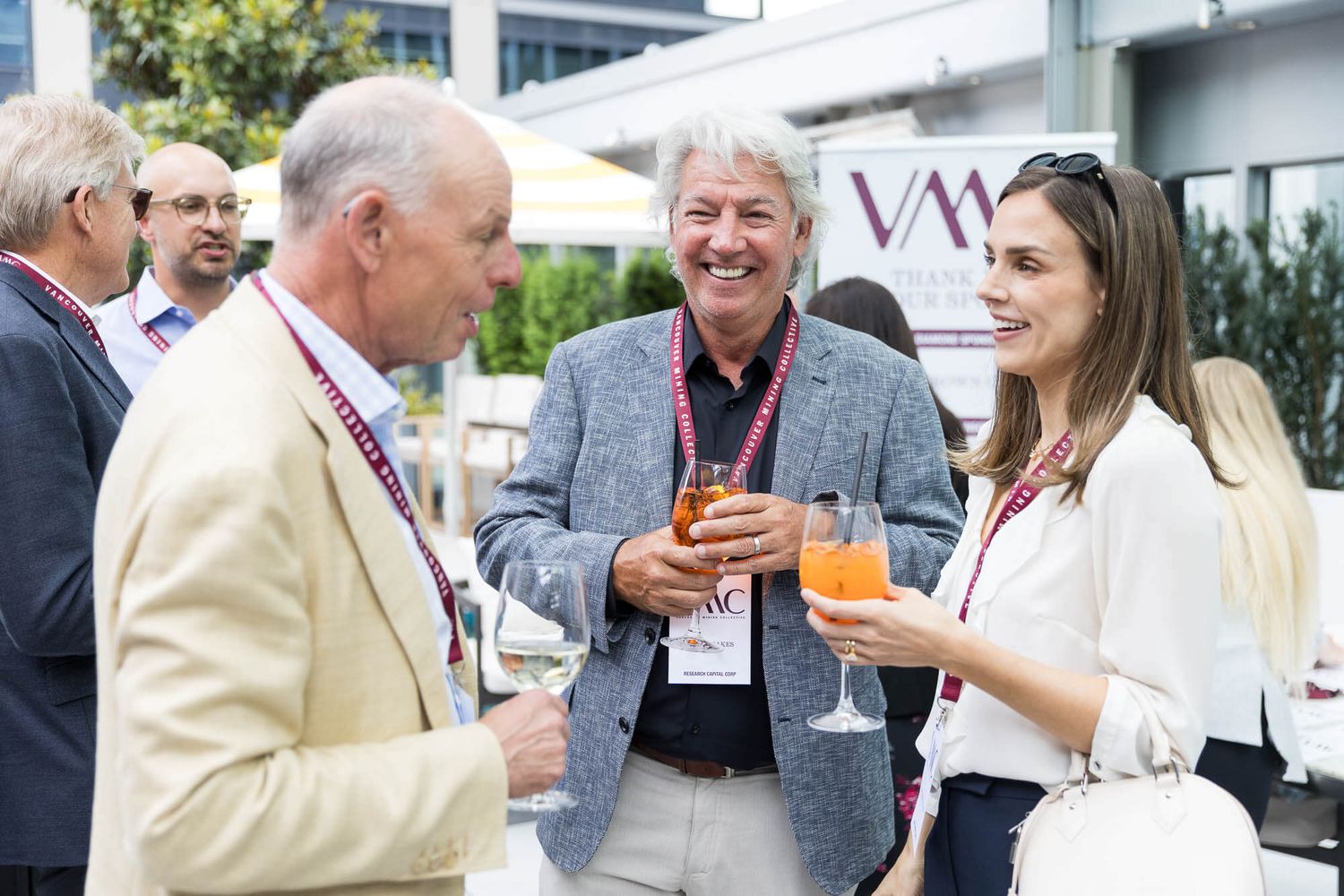 Three professionals networking at a corporate event, smiling and holding wine glasses outdoors.