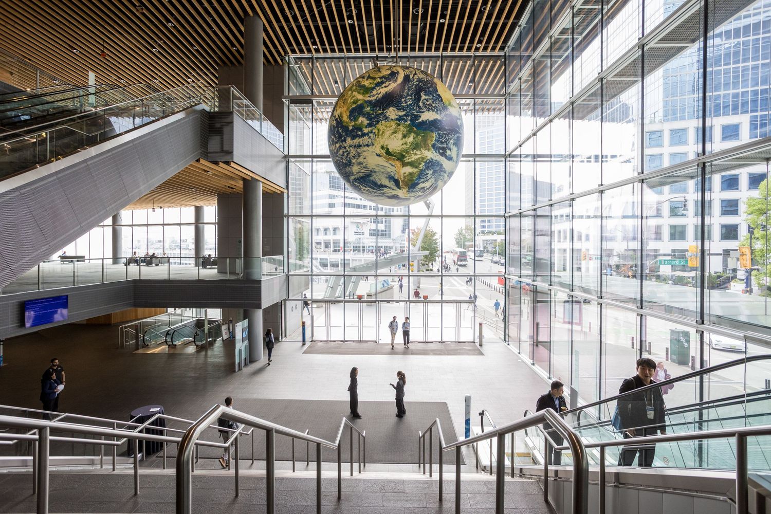 Modern building interior with a large illuminated Earth globe suspended in a bright atrium with glass walls and staircases.