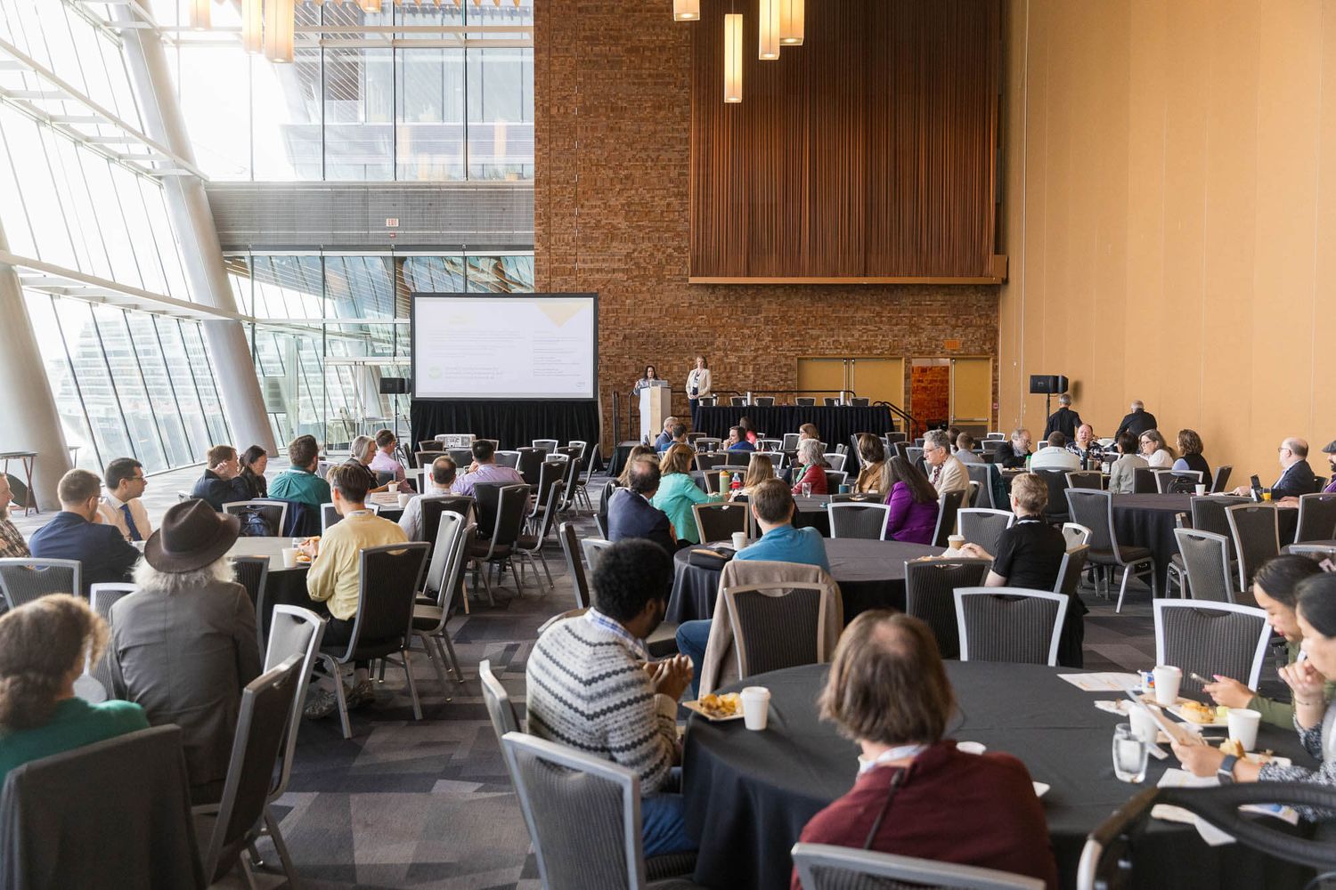 Large audience seated at round tables during a plenary session in the Vancouver Convention Centre.