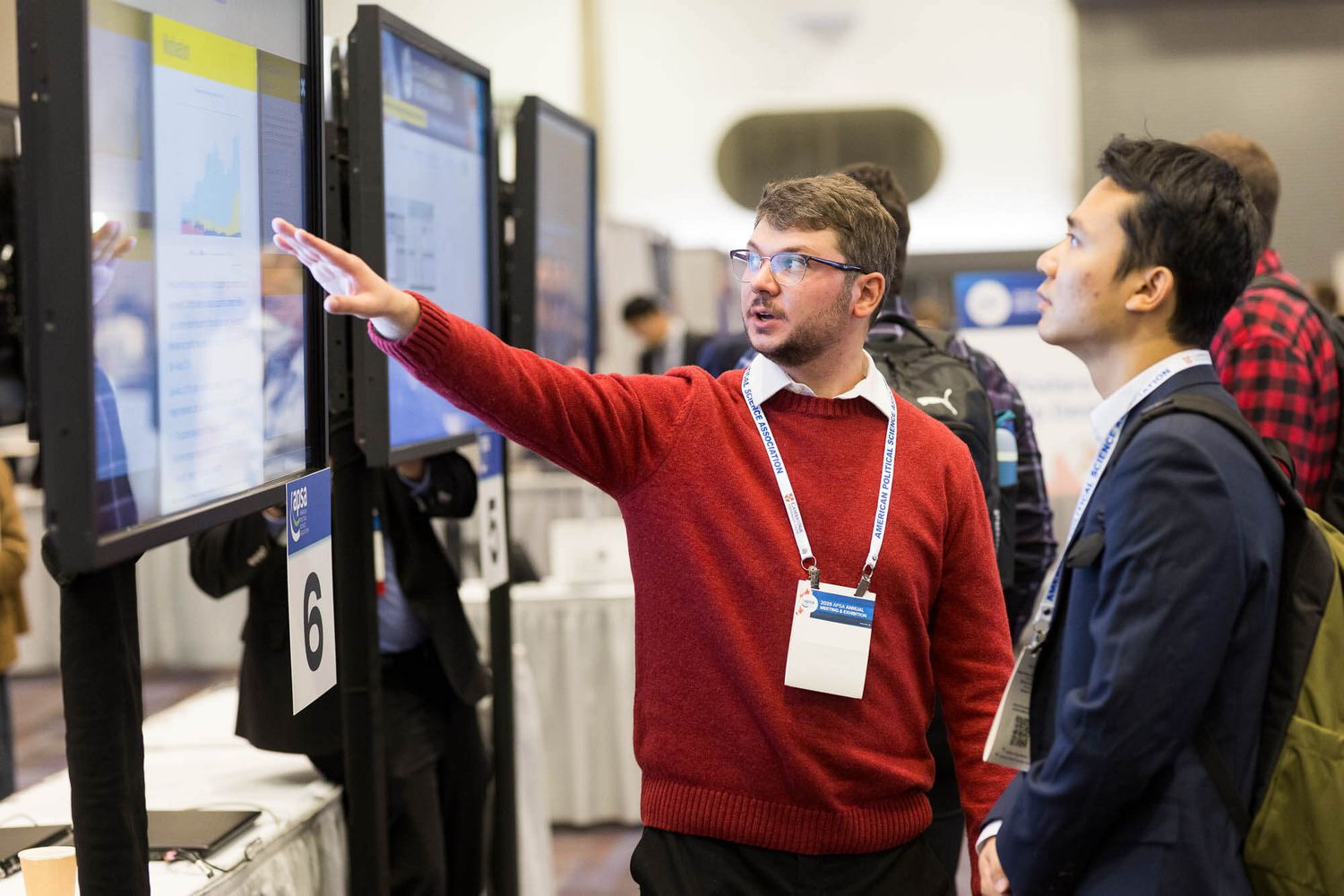 Two professionals examining a digital display screen at a tech conference exhibition, with one pointing at the monitor.