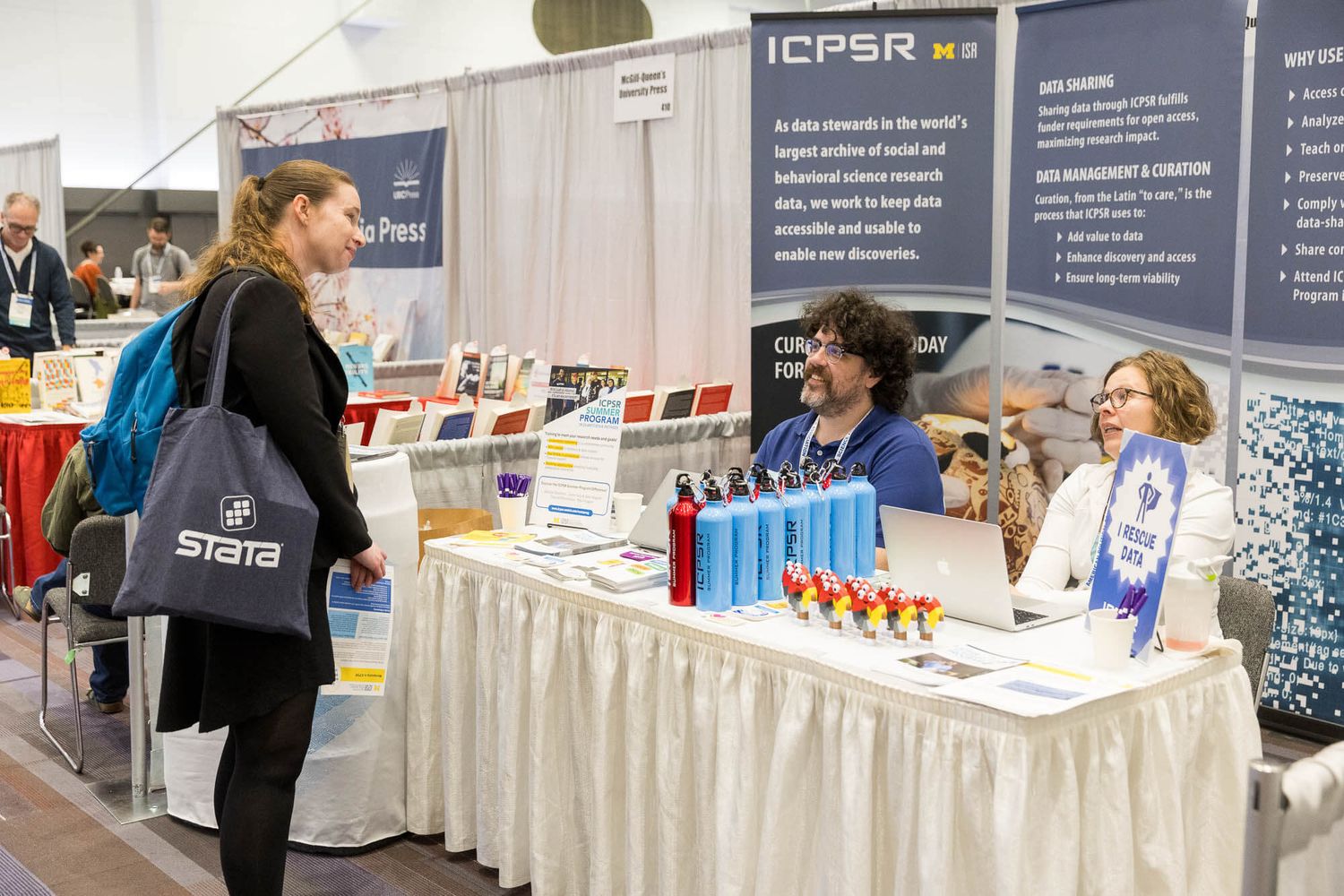 Attendees browse the ICPSR booth at an academic conference exhibition hall with Stata branded bags inside the Vancouver Convention Centre.