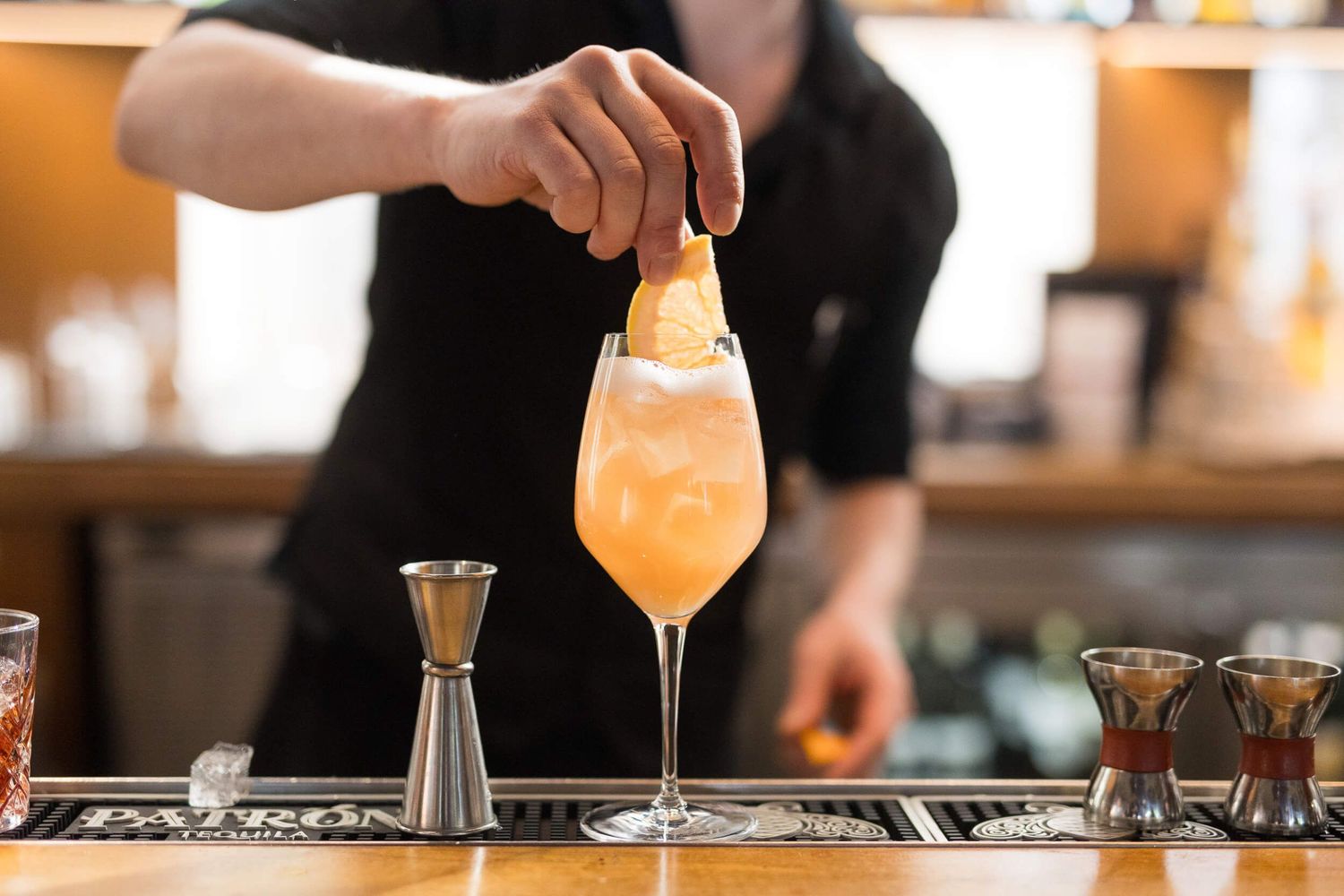 Bartender garnishing an orange cocktail in a stemmed glass with a citrus twist at a bar at D6 Lounge Vancouver.