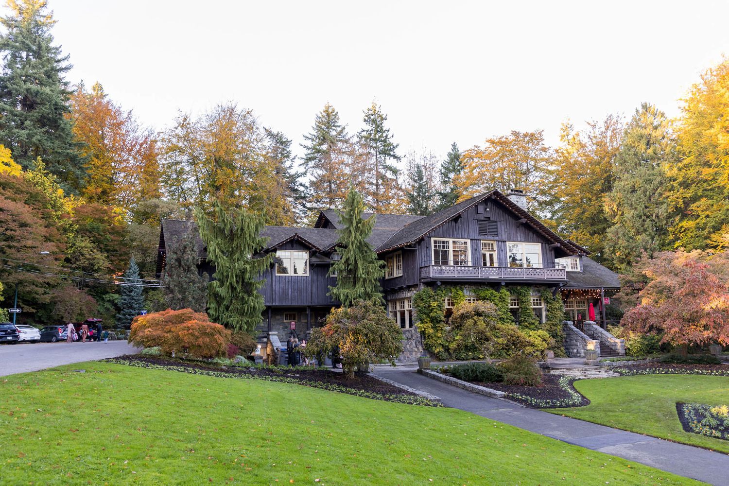 Dark wood craftsman home surrounded by lush autumn foliage and manicured green lawn in a serene forest setting.