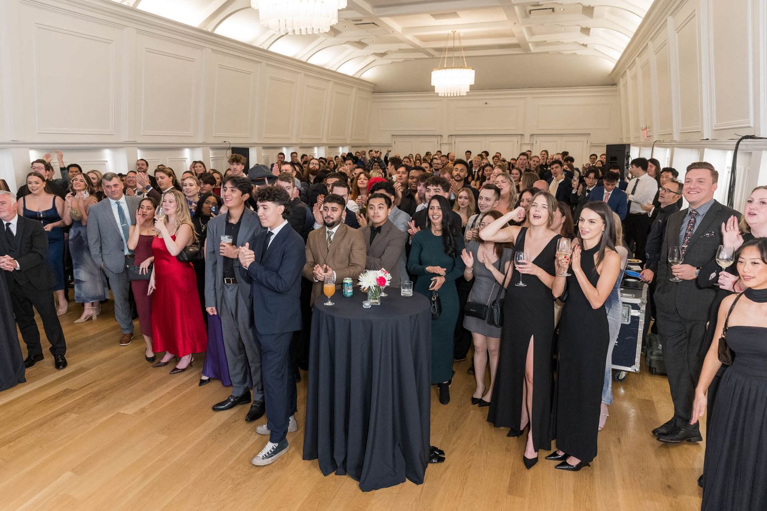Elegantly dressed guests applaud at a formal gala event in a grand ballroom venue.