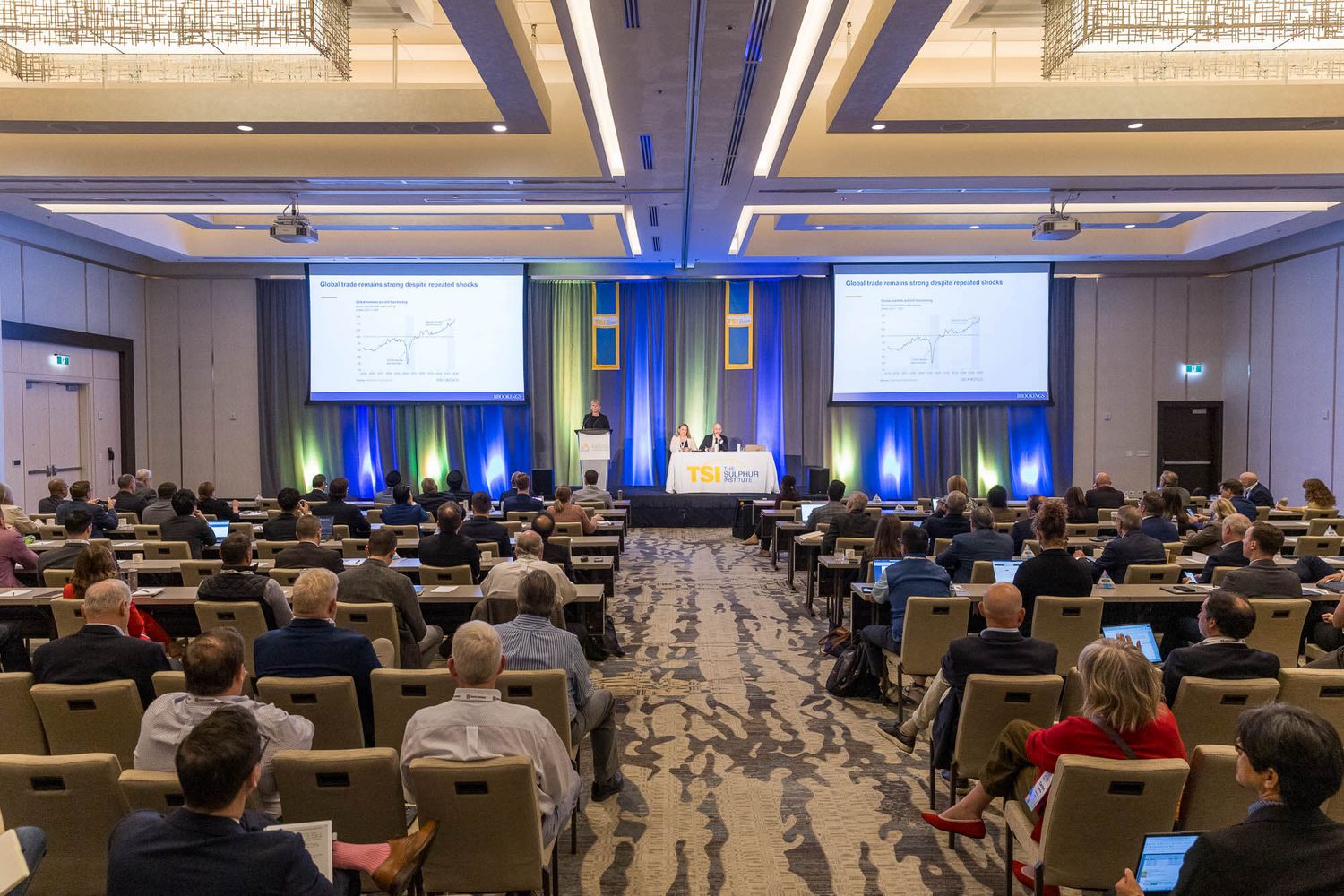 Large conference room filled with attendees watching presentations on multiple screens during a professional business event.