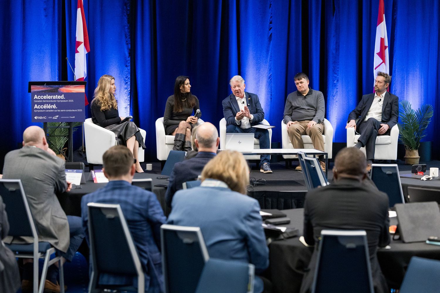 Panel discussion at a professional conference with five speakers on stage before an audience, Canadian flags in background.