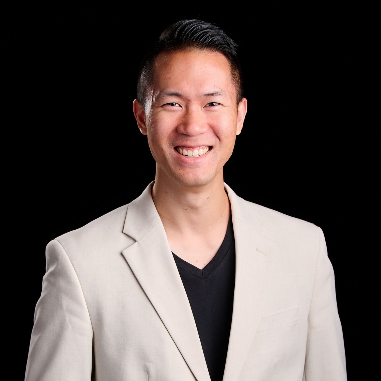 Raymond Chou in a light beige blazer and black V-neck shirt posing against a dark background.