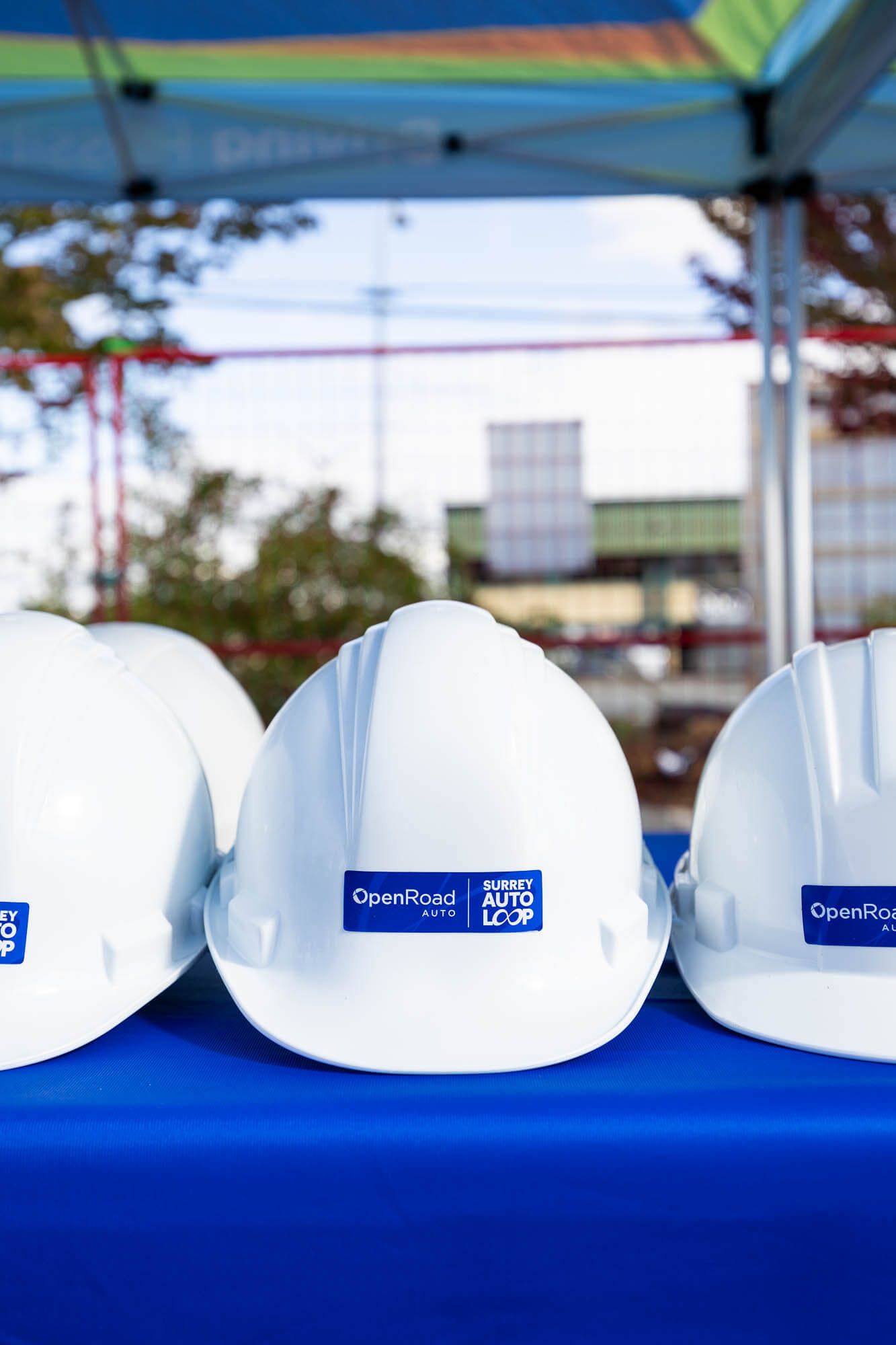 White OpenRoad Auto hard hats displayed on a blue table at a construction groundbreaking ceremony outdoors.