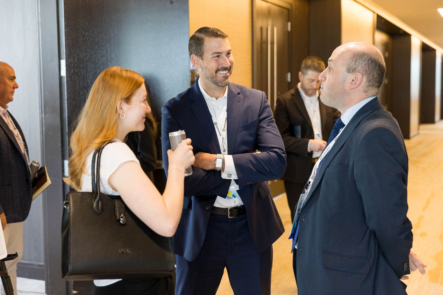 Three business professionals networking and conversing in a conference hallway during a corporate event.