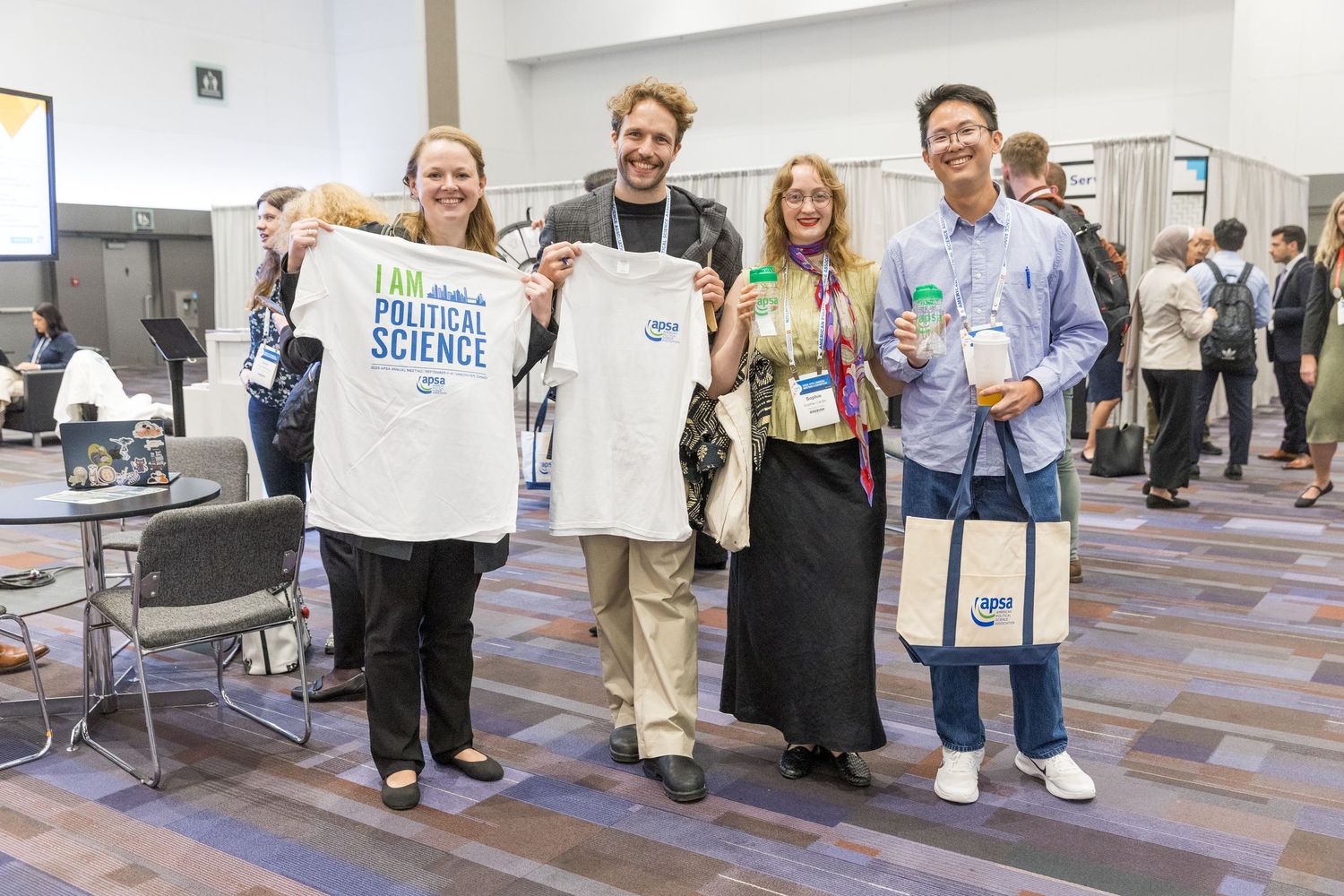 Four smiling conference attendees pose together, one holding a Political Science t-shirt at an academic event.