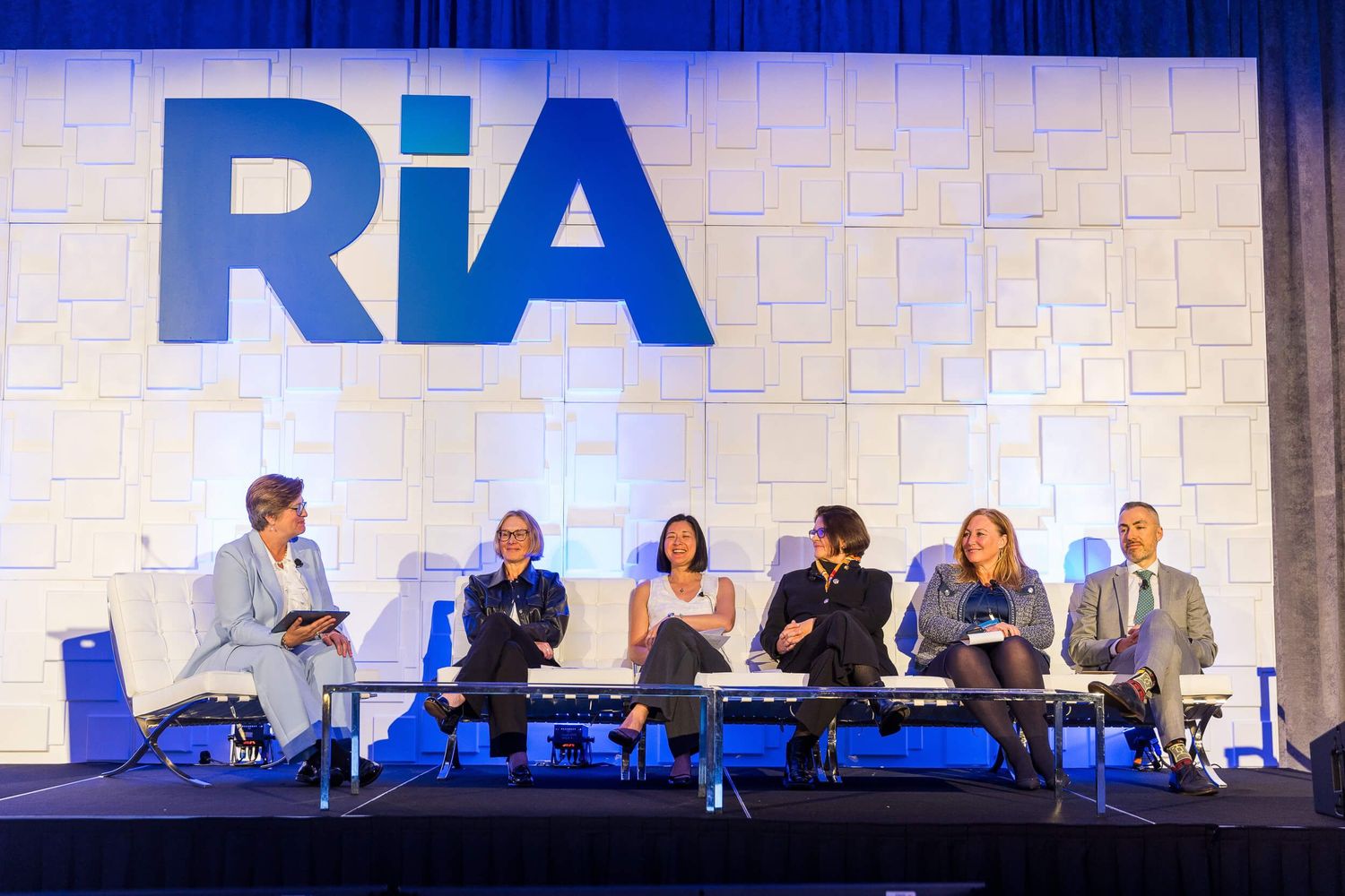 Six panelists speak on stage beneath a large RiA logo at a professional conference event at the Sheraton Wall Centre Vancouver.