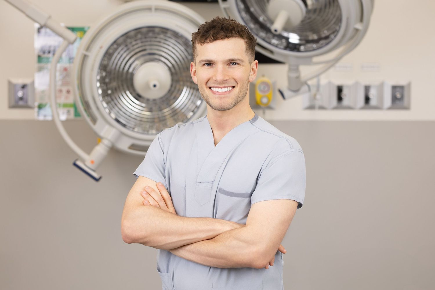 Smiling male healthcare professional in gray scrubs with arms crossed inside an O.R. room at Vancouver General Hospital.