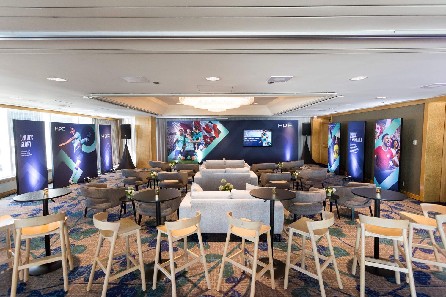 Modern sports lounge with bar stools, tables, and large screen displaying soccer content for corporate event.