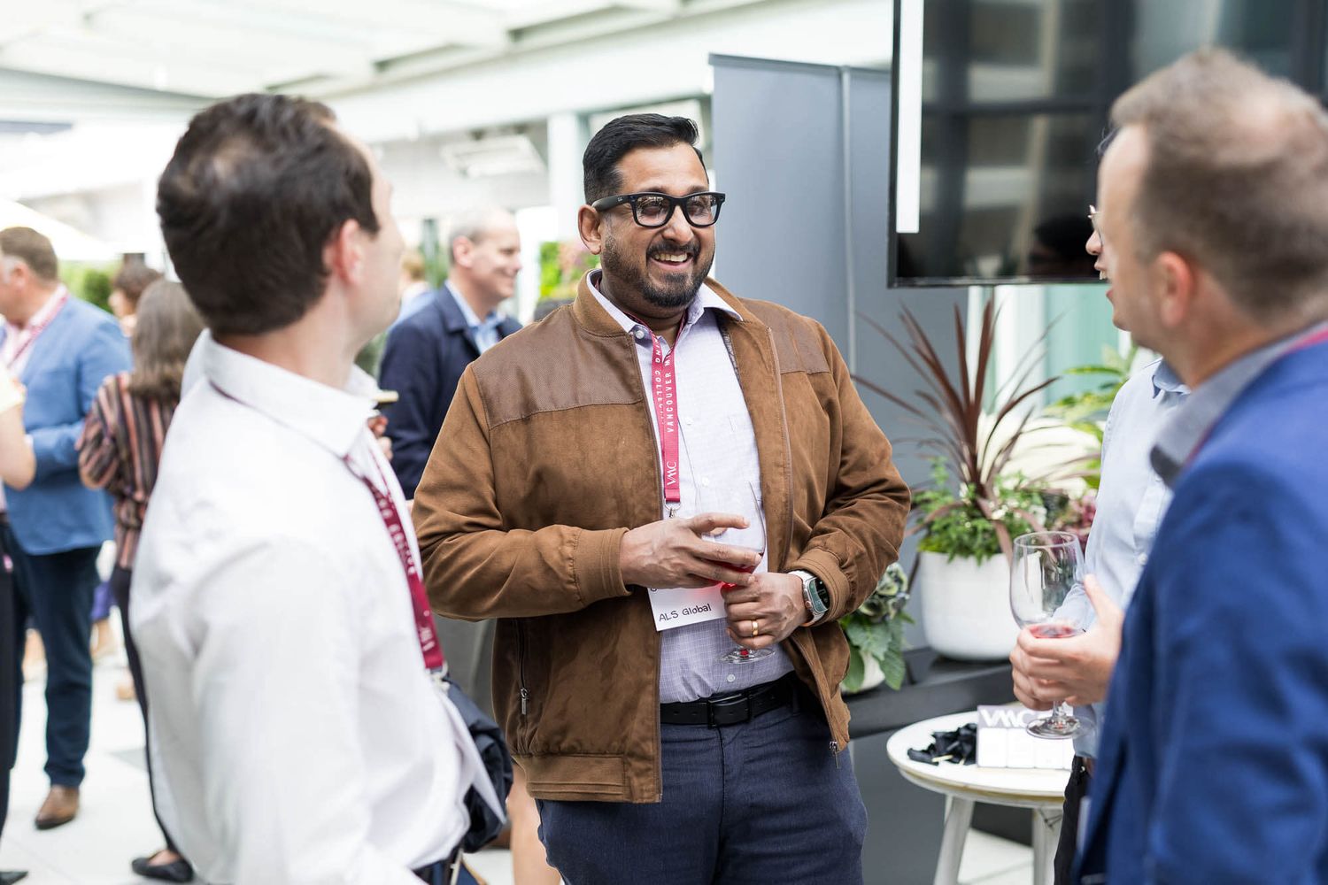 Smiling man in brown jacket networking with colleagues at a professional outdoor business event.