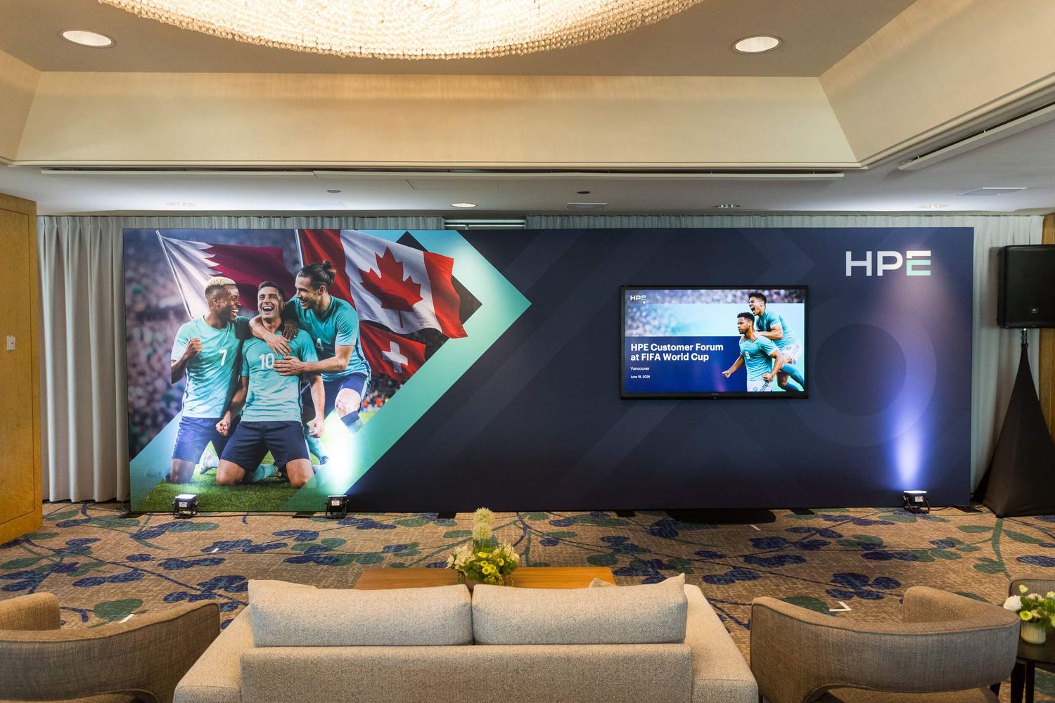 HPE branded lounge with soccer-themed mural, flat screen TV, and elegant seating area at a corporate event.