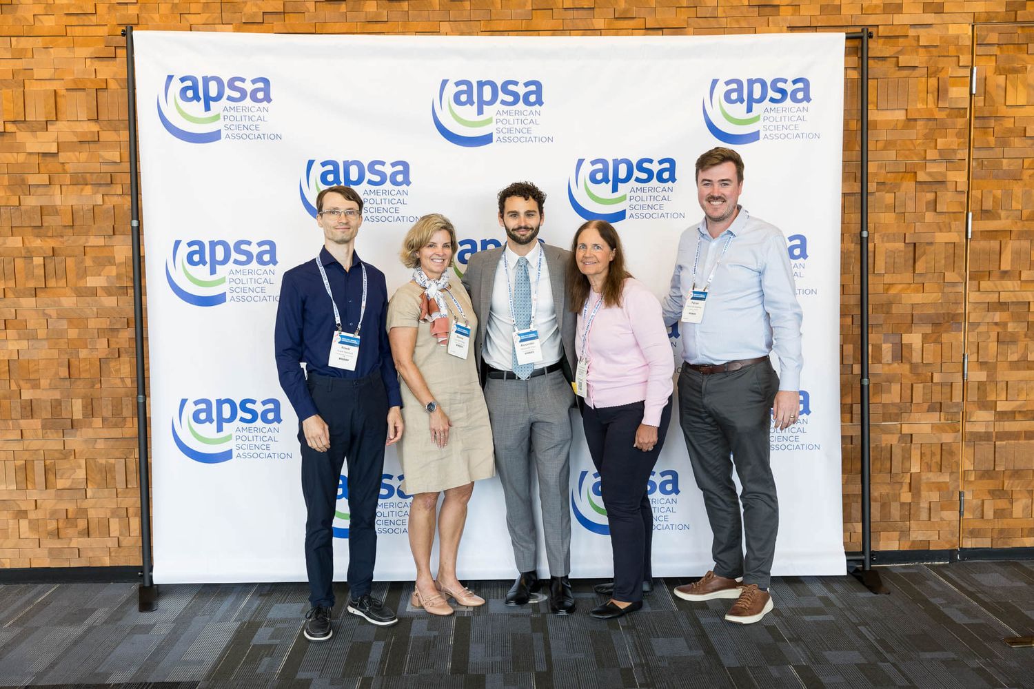 Five professionals posing together in front of an APSA conference backdrop at a corporate event at the Vancouver Convention Centre.