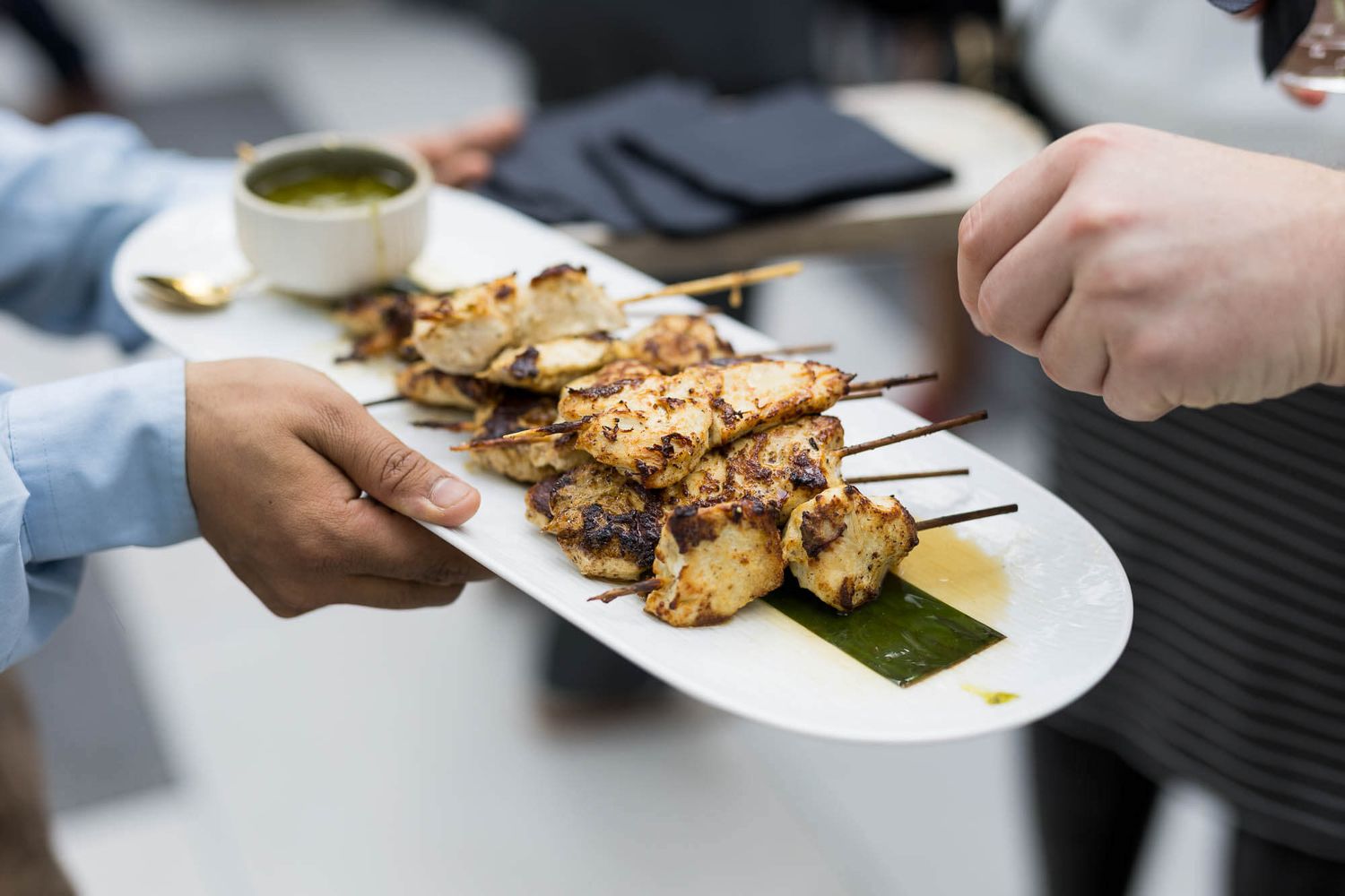 Grilled chicken skewers on a white plate served with green dipping sauce at a restaurant.