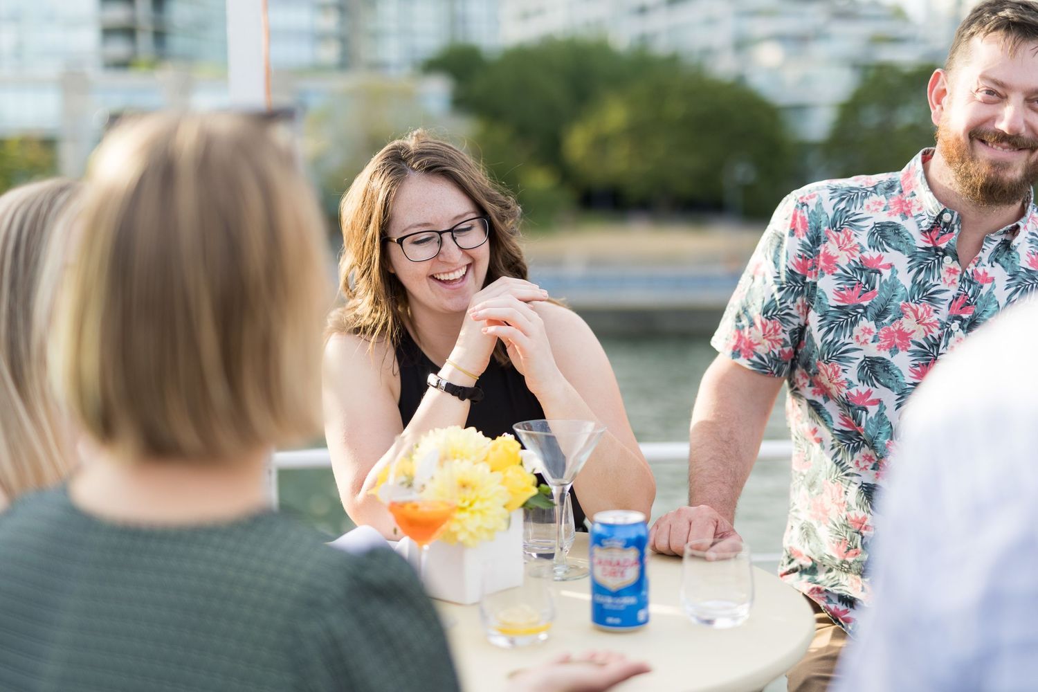 Woman with glasses laughing at outdoor rooftop gathering with friends and drinks on table at Pacific Yacht Charters.