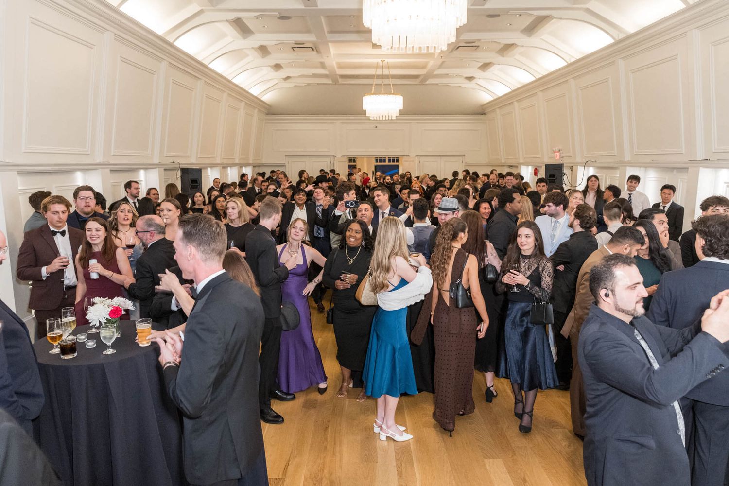 Elegant formal gala event with guests dancing and socializing in a grand ballroom with chandeliers.