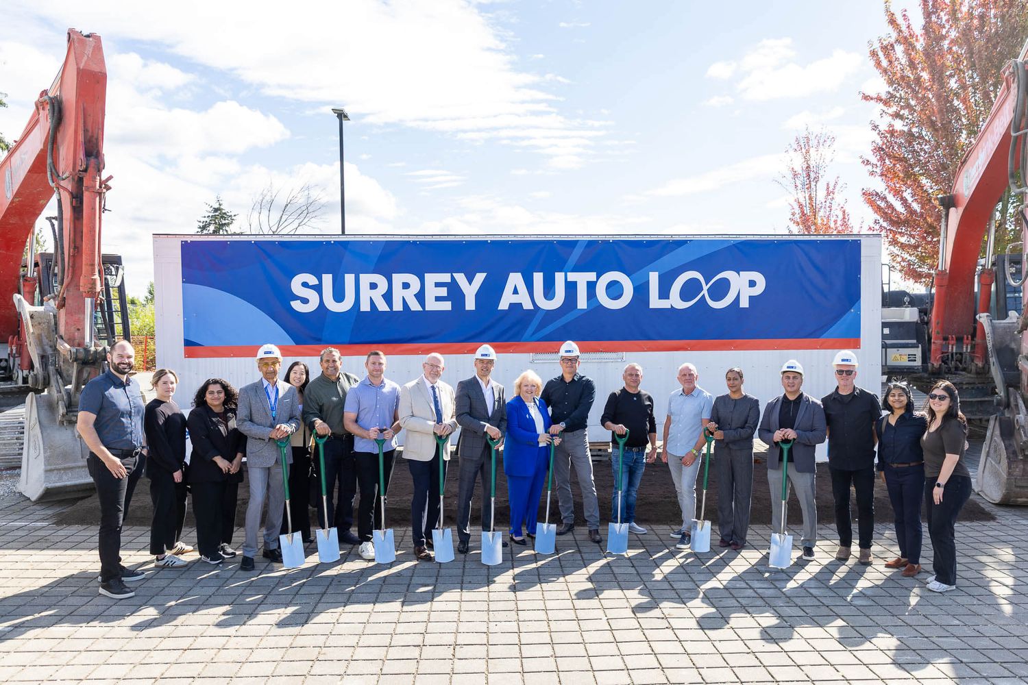 Surrey Auto Loop groundbreaking ceremony with team holding shovels in front of branded banner outdoors.