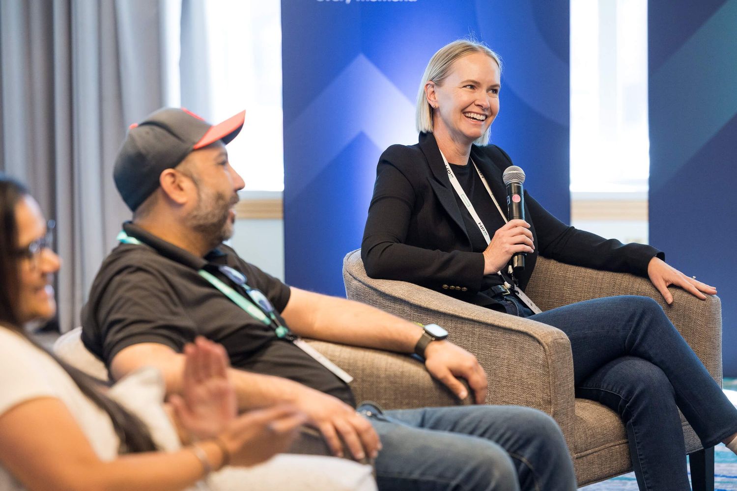 Three panelists engage in lively discussion at a conference, with a woman holding a microphone and smiling on stage.