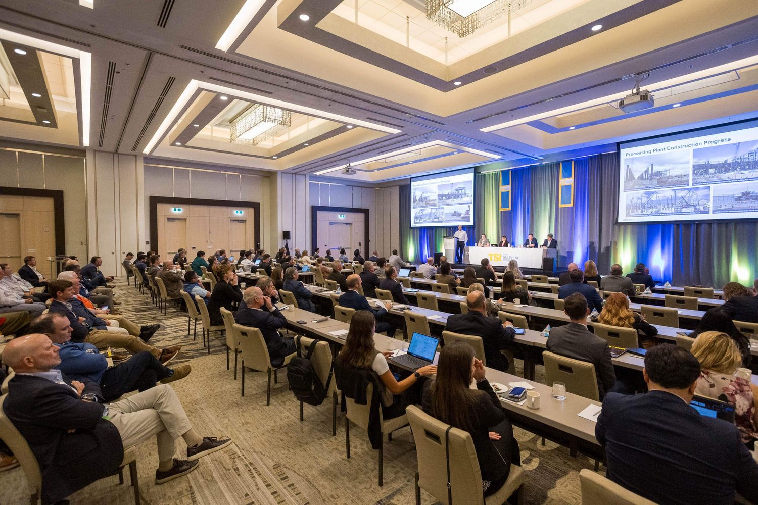 JW Marriott Parq Vancouver filled with attendees seated at rows of tables facing a panel of speakers and large presentation screens.