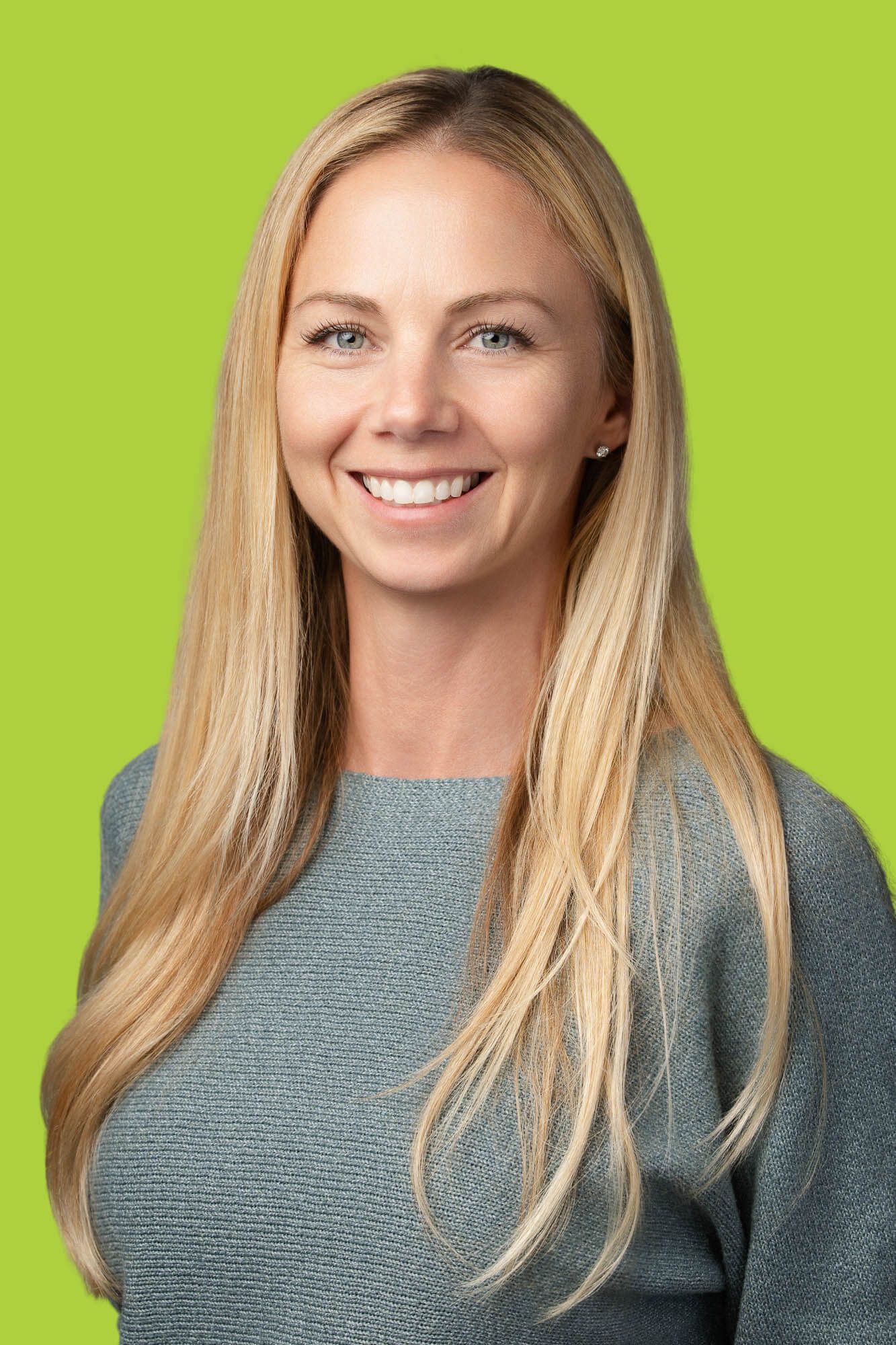 Smiling blonde woman in a gray top poses for a professional headshot against a bright green background.