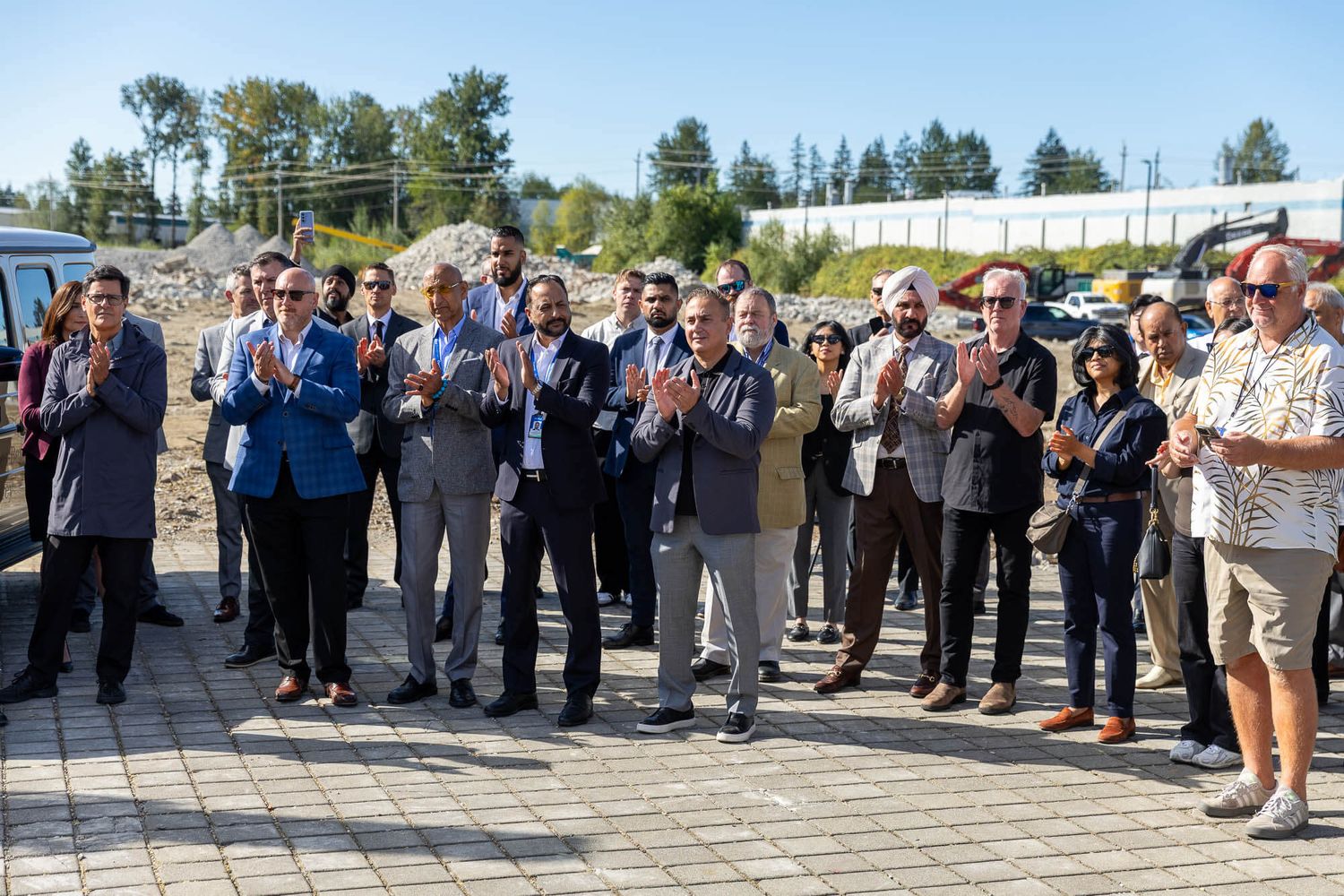 Group of professionals applauding outdoors at a groundbreaking ceremony on a sunny day.