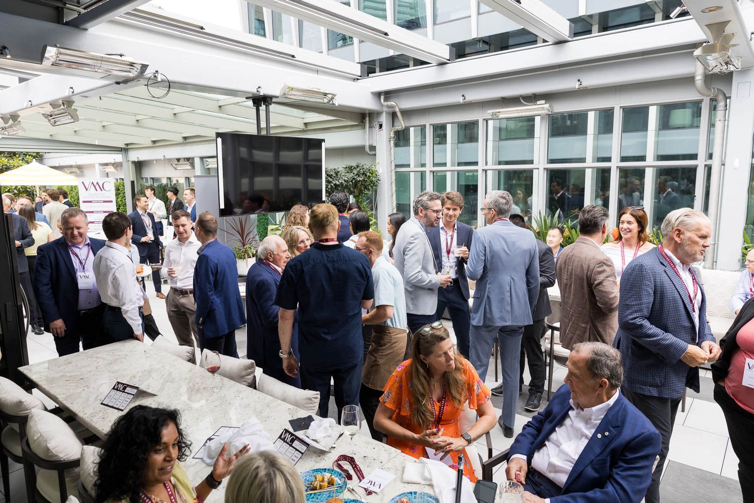 Large group of business professionals mingling at an outdoor corporate networking event on a terrace.