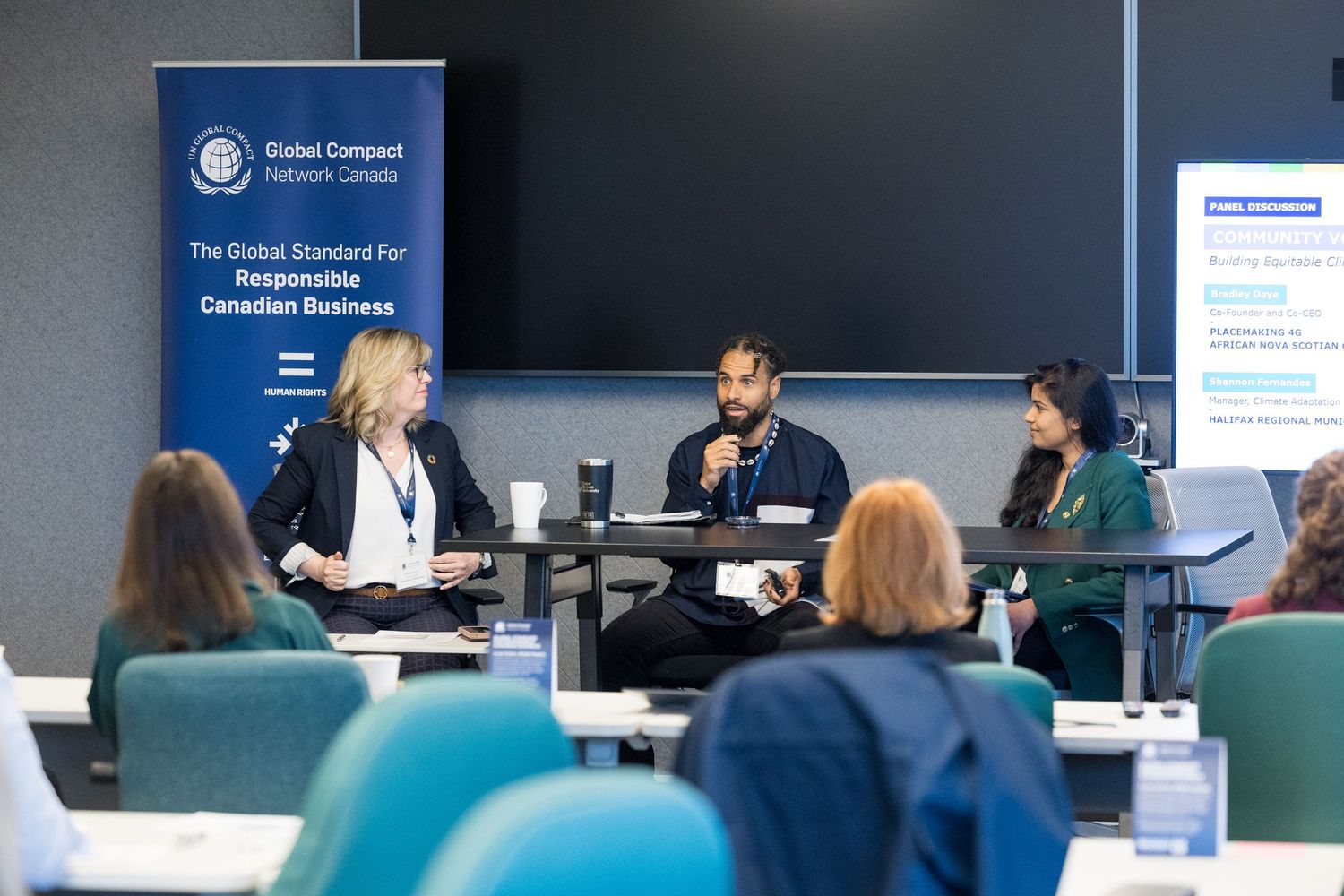 Panel discussion at Global Compact Network Canada event with three speakers seated at a table in a conference room.