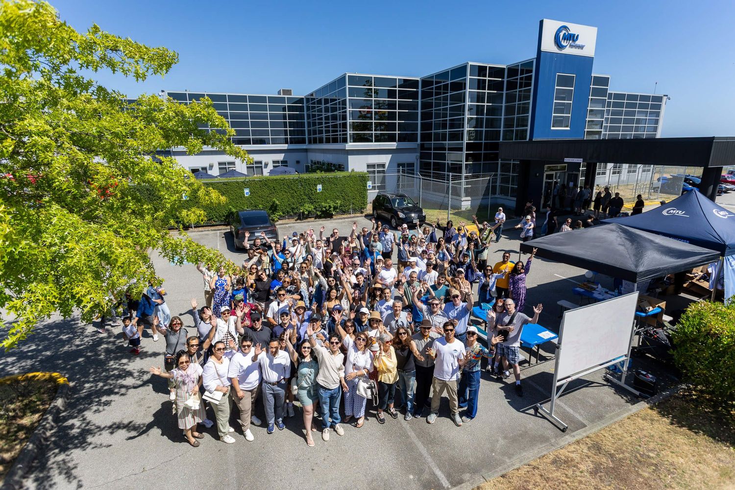 Large group of employees gathered outside a modern corporate office building on a sunny day for a company event.