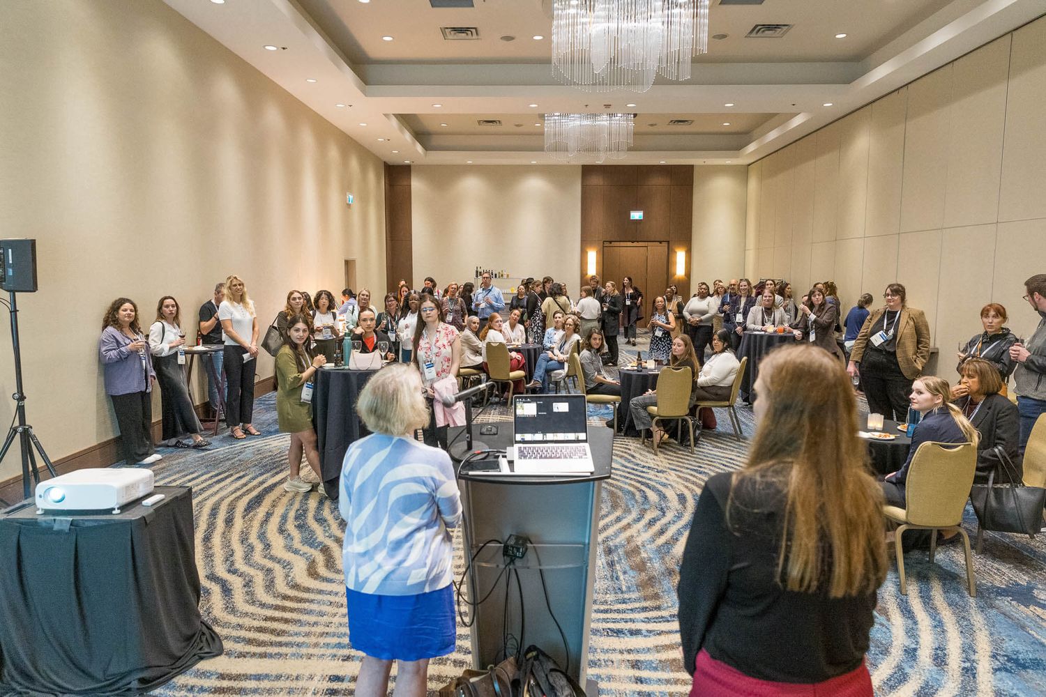 Large group of women attending a professional conference in an elegant hotel ballroom with chandelier lighting.
