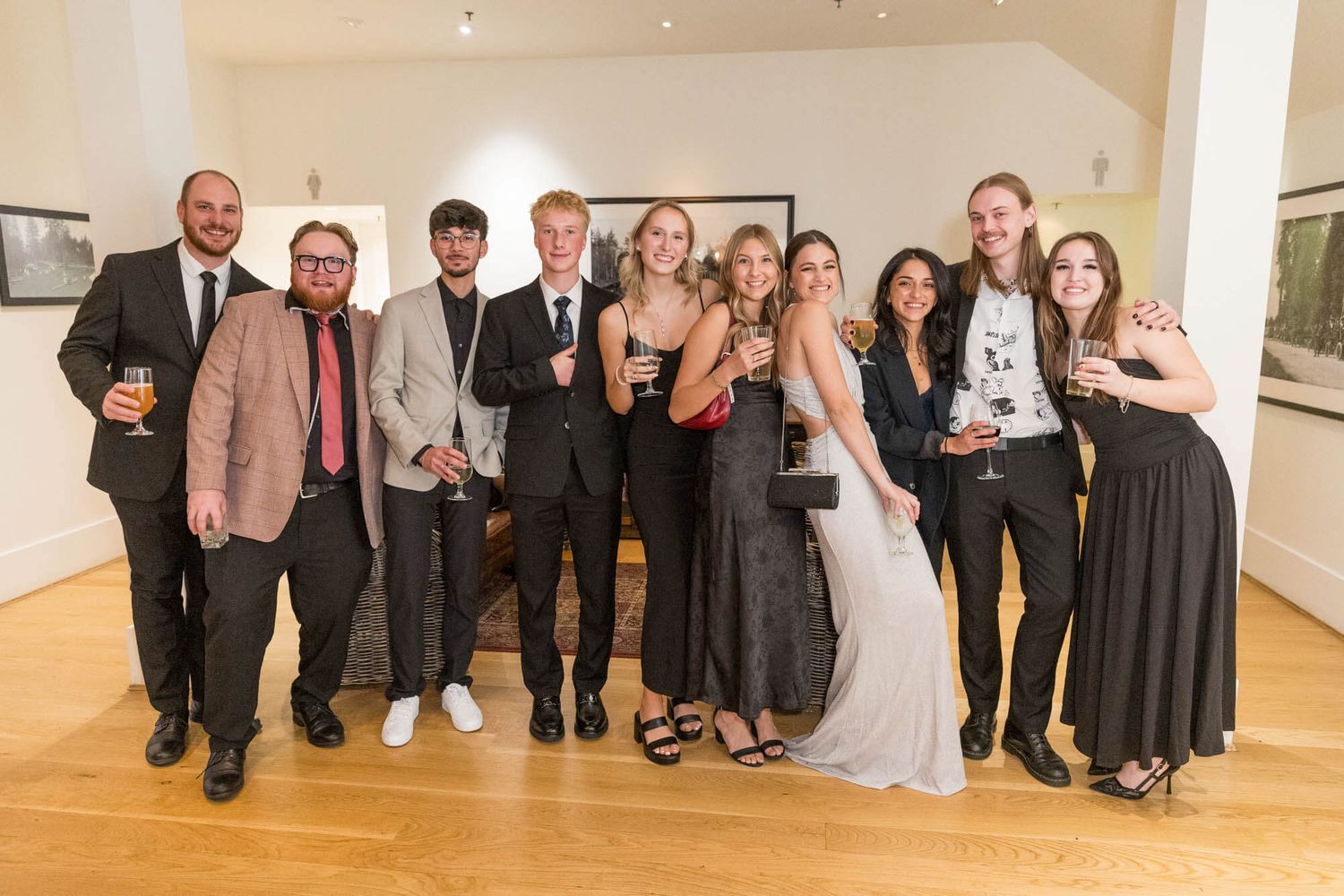 Group of elegantly dressed young adults posing together at a formal event in a well-lit gallery space.