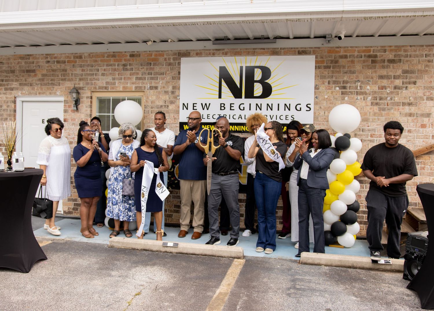 Group celebrates ribbon cutting at New Beginnings Technical Services grand opening with balloons and signage.
