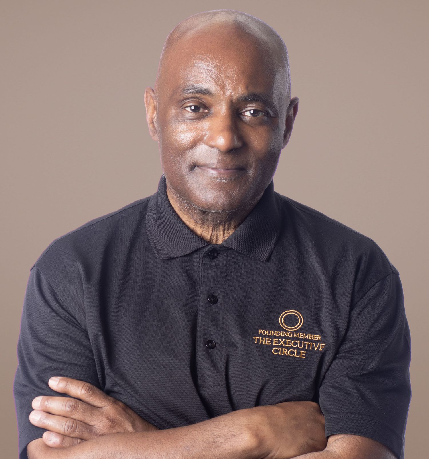 Professional man with crossed arms wearing a black Executive Circle polo shirt, posing confidently against a neutral background.