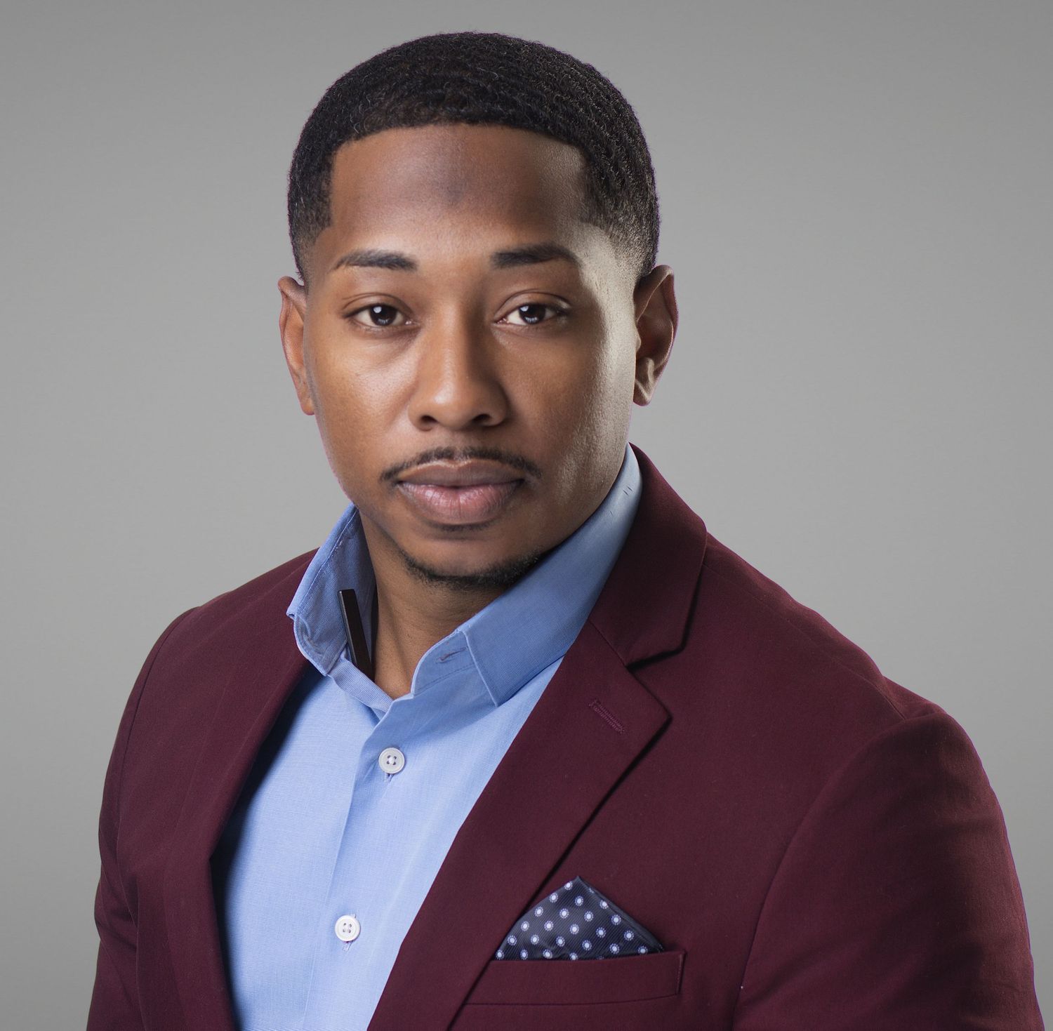 Professional man in burgundy blazer and light blue shirt with pocket square poses for a formal portrait.