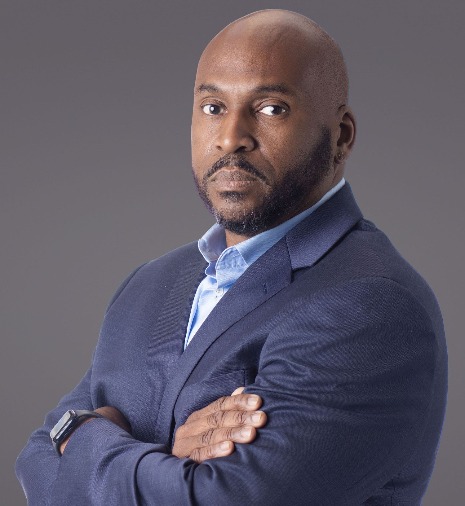 Professional man in navy suit with arms crossed, confident pose against gray background.