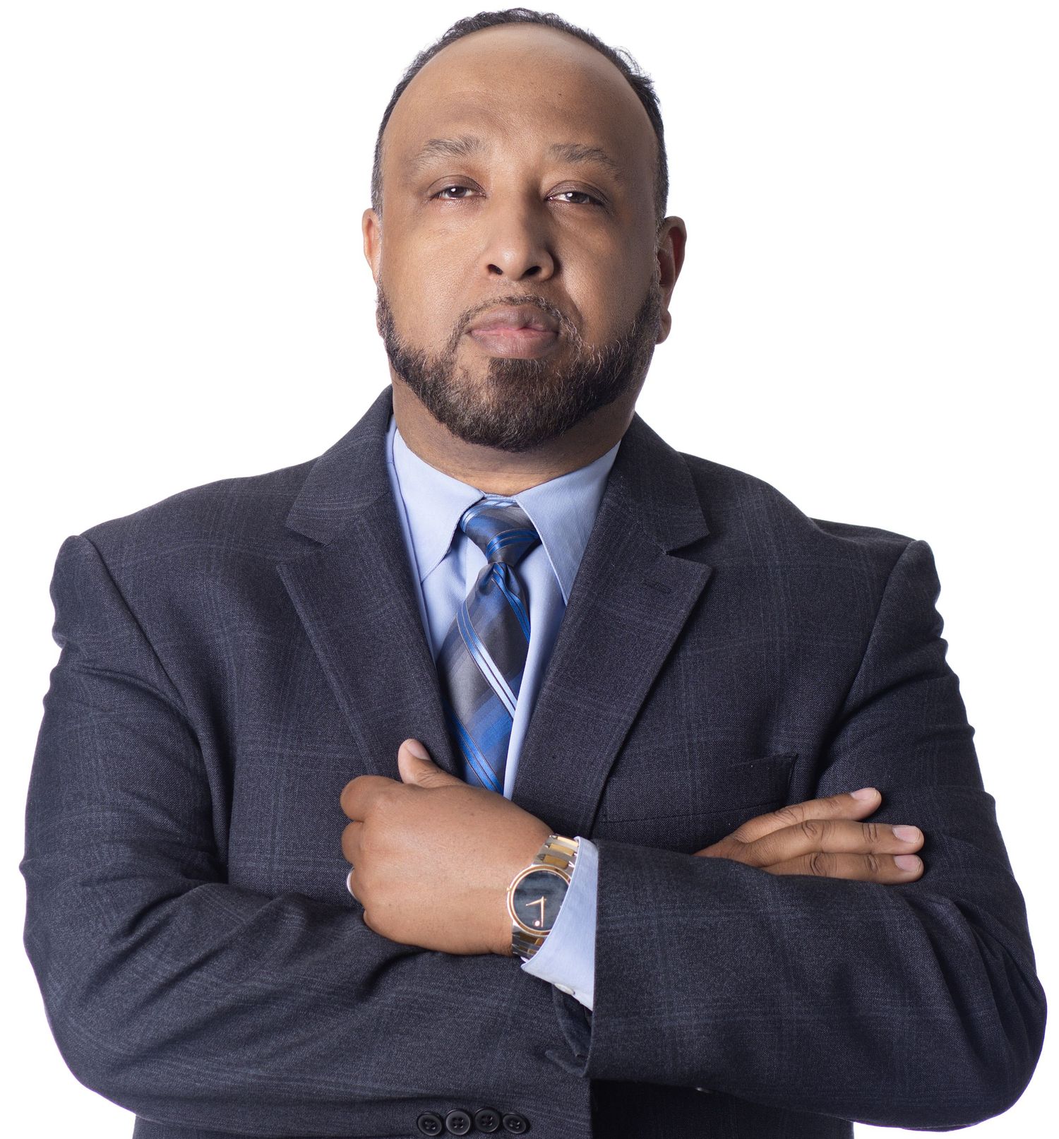 Professional man in dark suit and blue tie stands with arms crossed against white background.